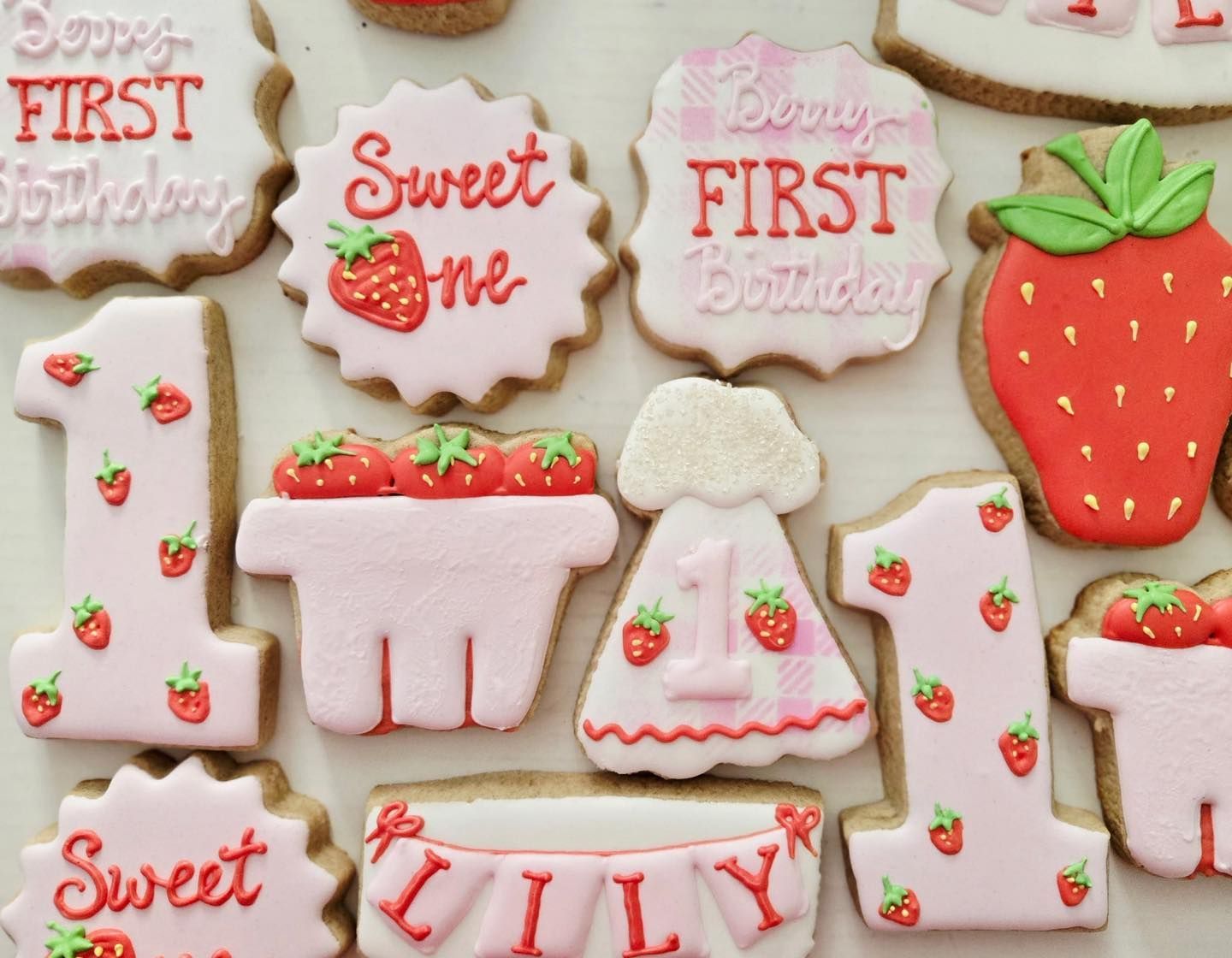 Decorated sugar cookies with strawberry theme for a first birthday. Pink and white frosting with red strawberries.