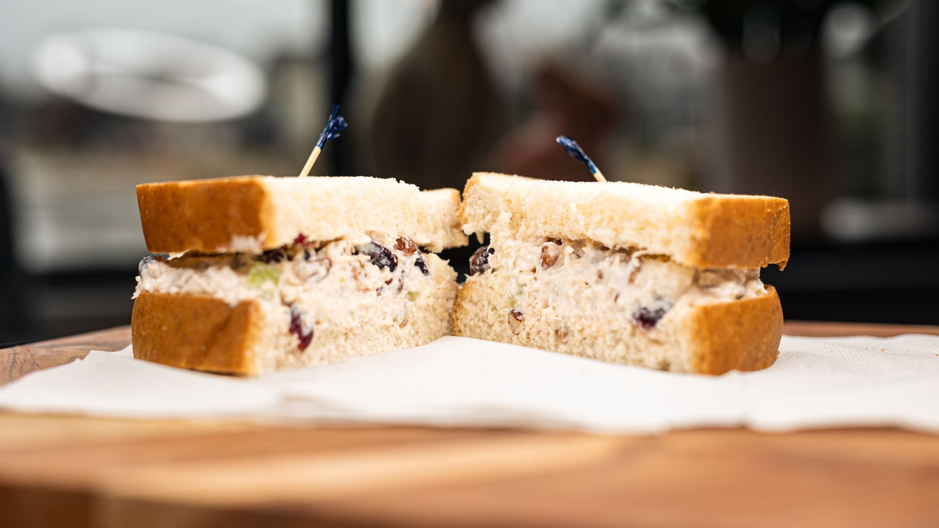 Chicken salad sandwich cut in half, on a white napkin, on a wooden board.