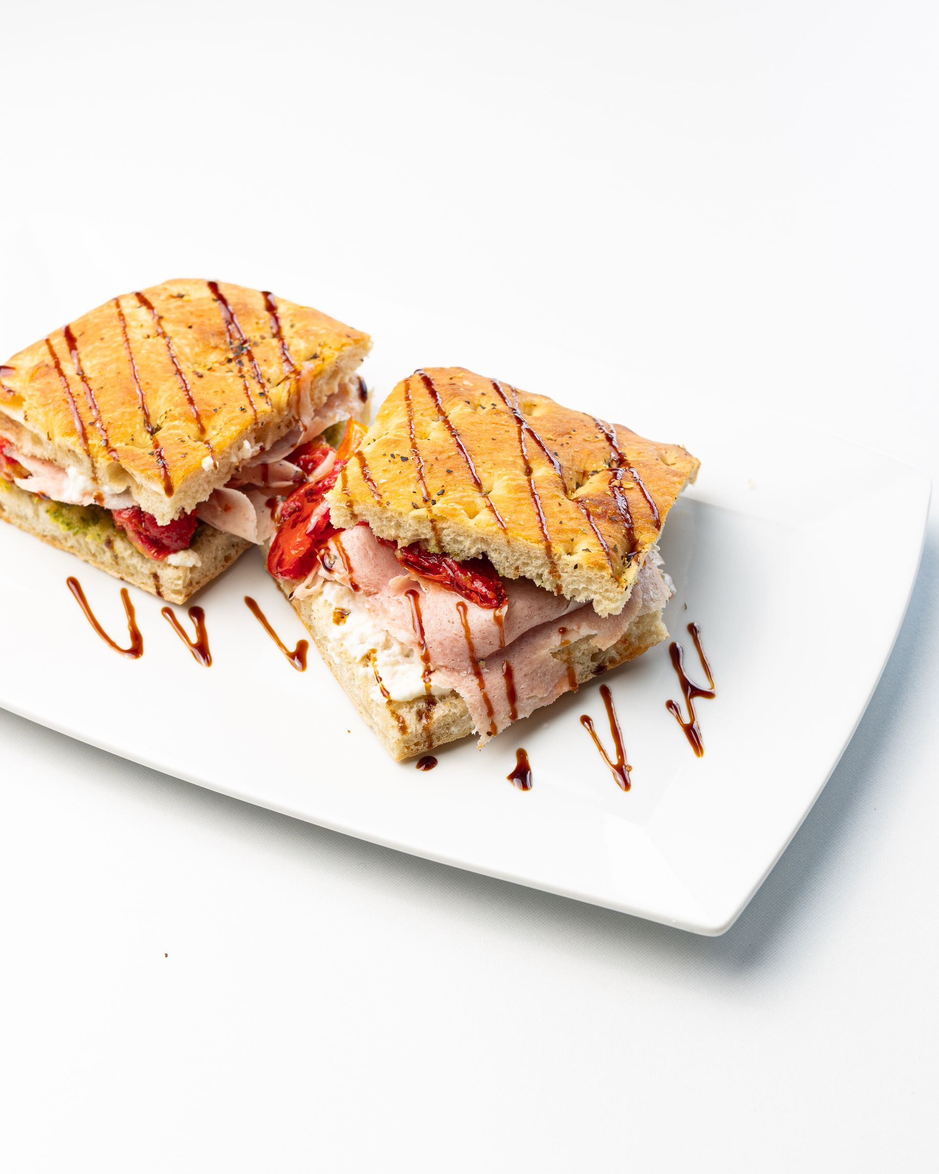 Two sandwiches on a white plate, drizzled with balsamic glaze.