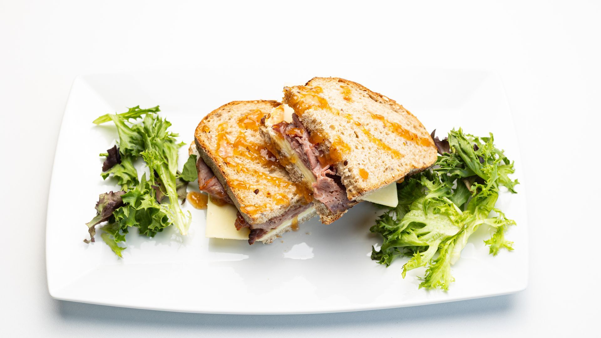 Grilled sandwich cut in half on a white plate with greens.