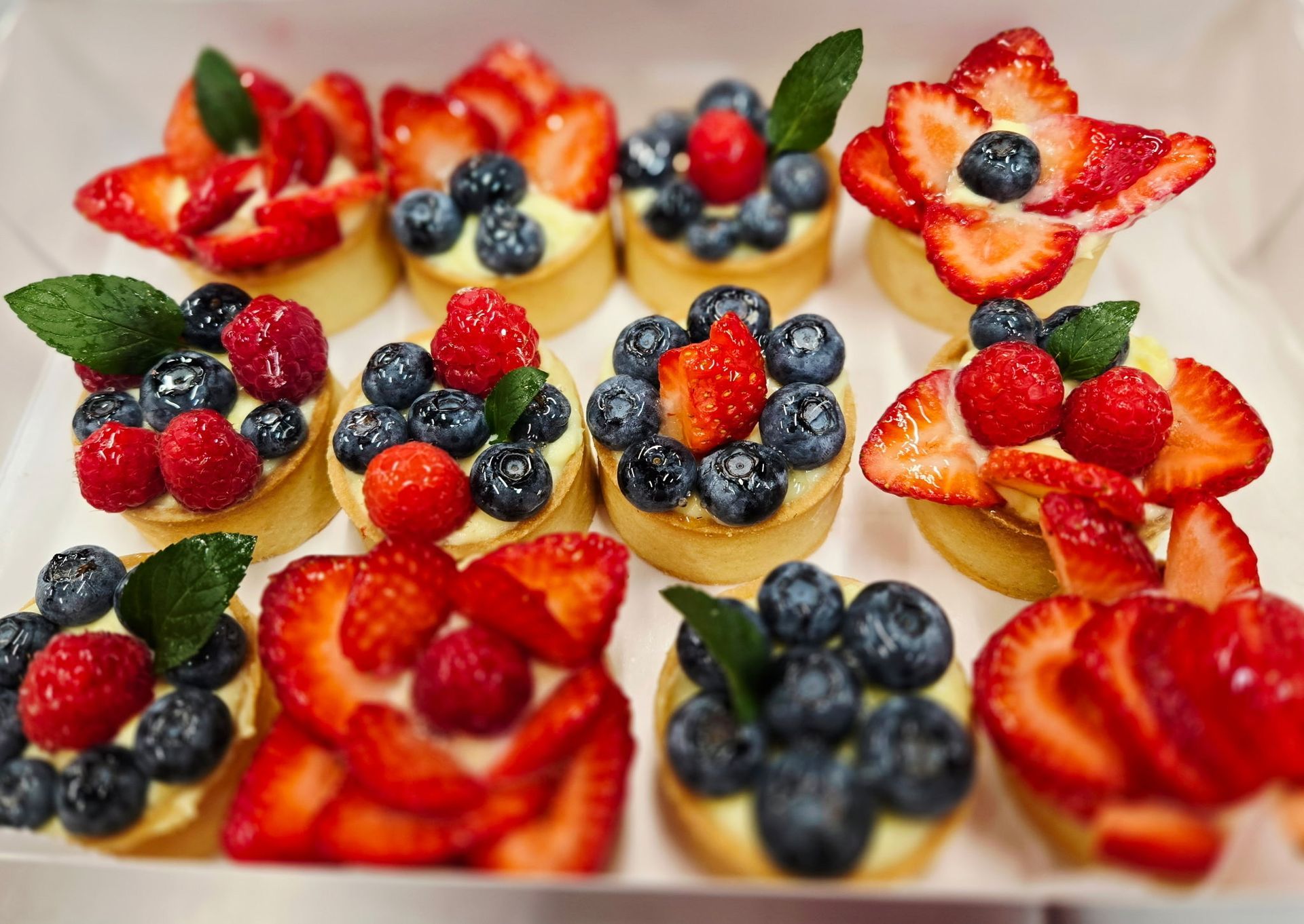 Fruit tarts: small pastries with assorted berries and strawberries, garnished with mint.