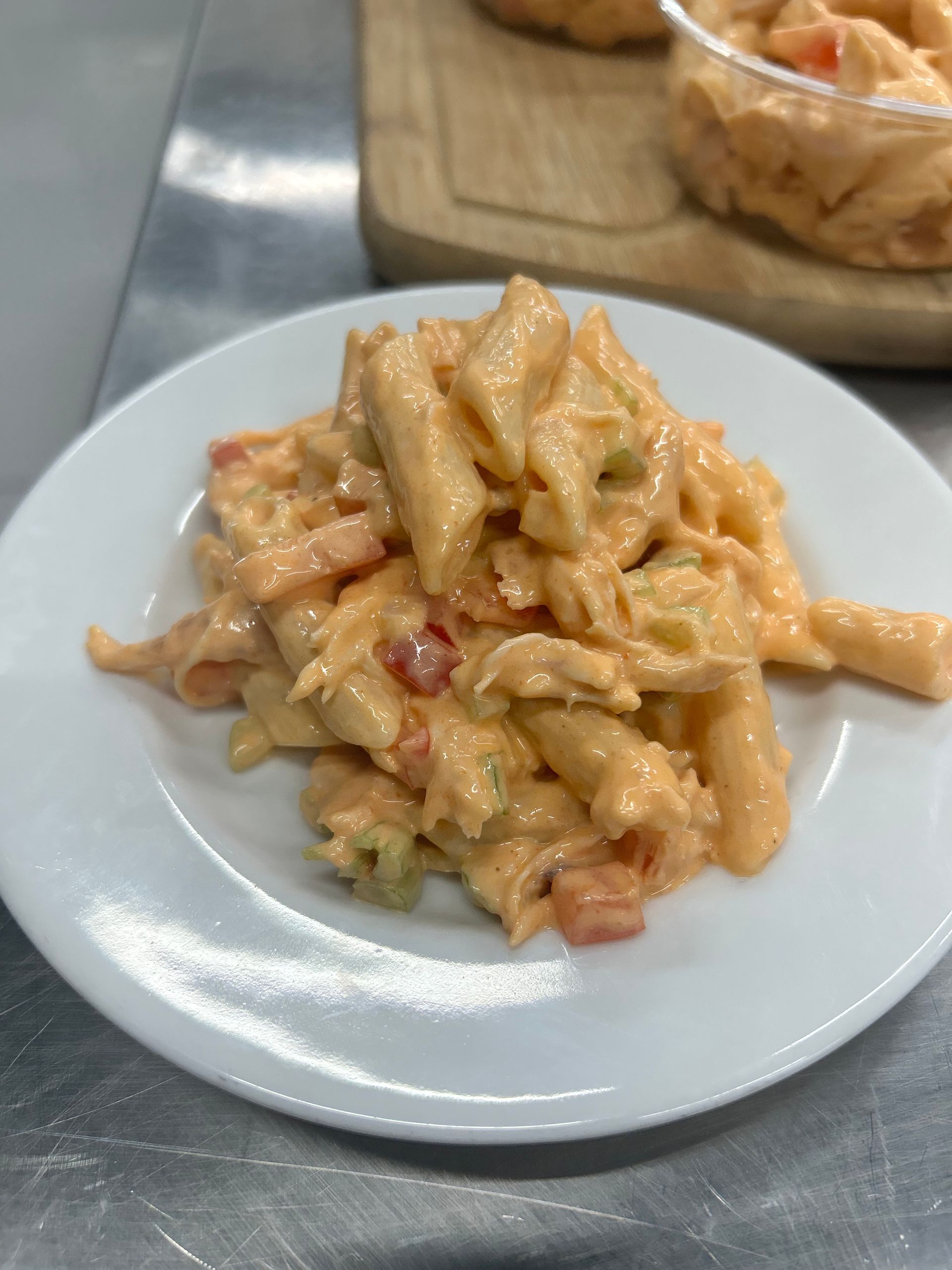 Pasta salad with orange sauce, celery, and tomatoes on a white plate.