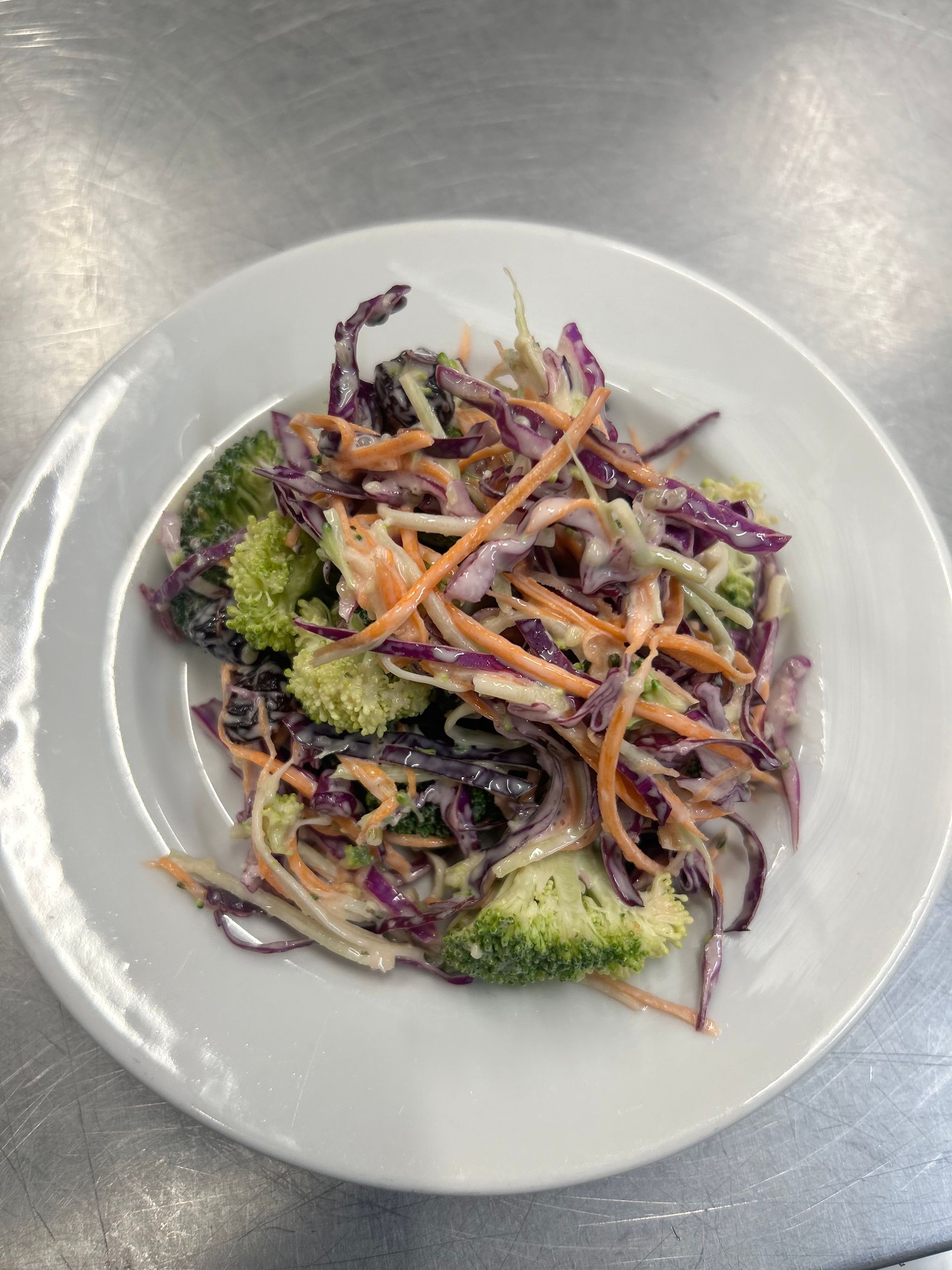 Coleslaw with broccoli, shredded carrots, and red cabbage on a white plate.