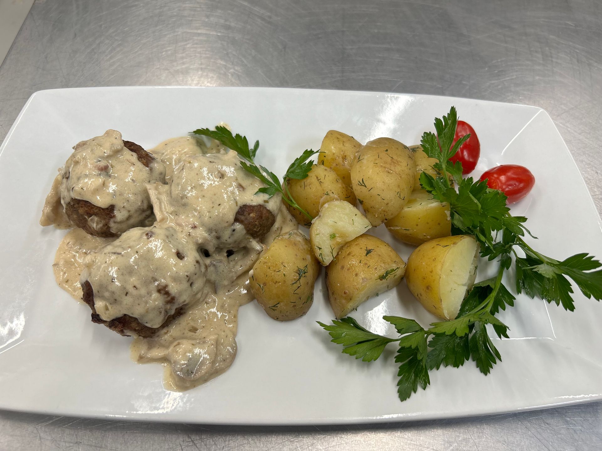 Meatballs in creamy sauce with roasted potatoes, parsley, and tomatoes on a white plate.