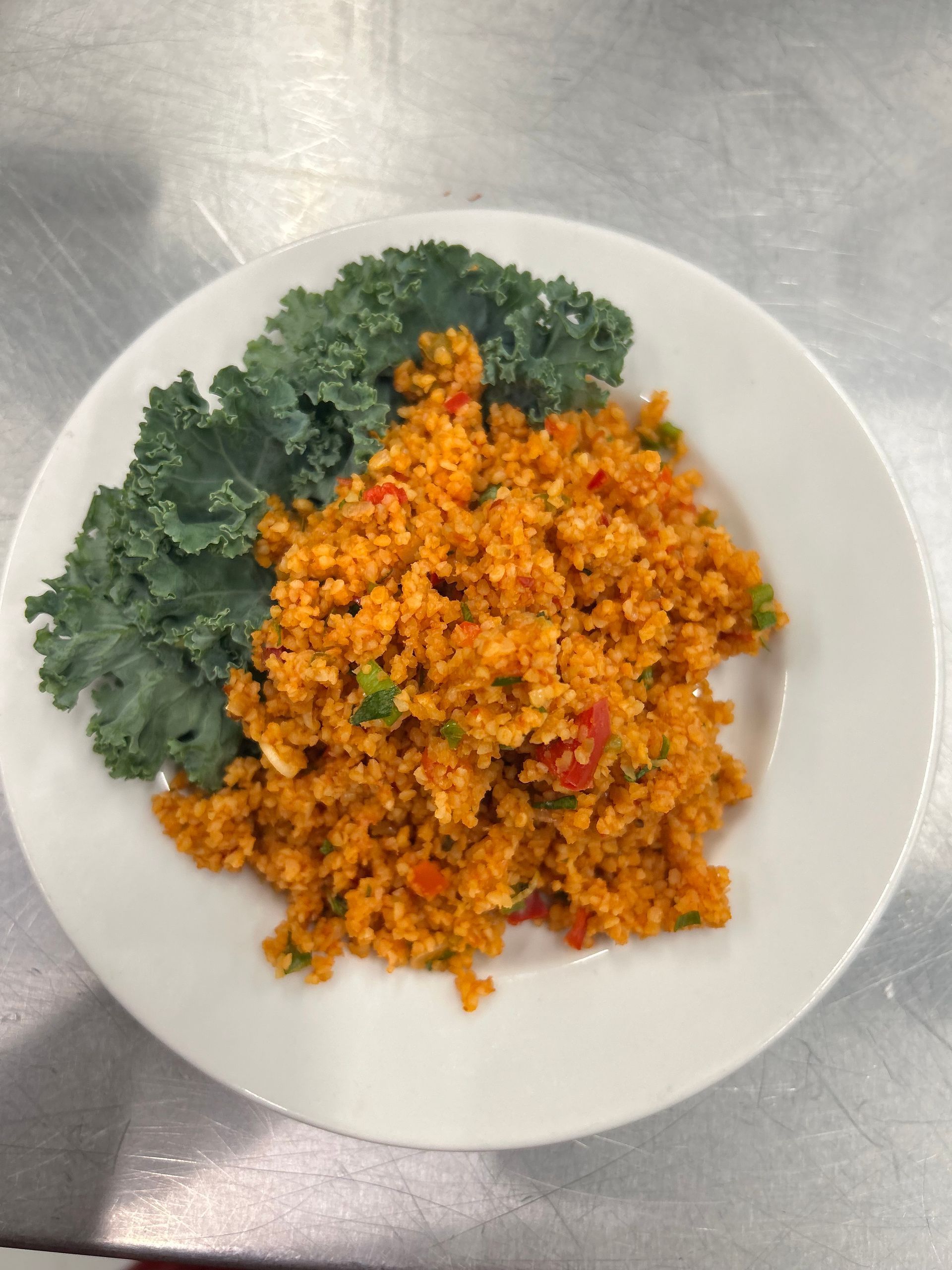 Orange grain dish with green vegetables on a white plate.