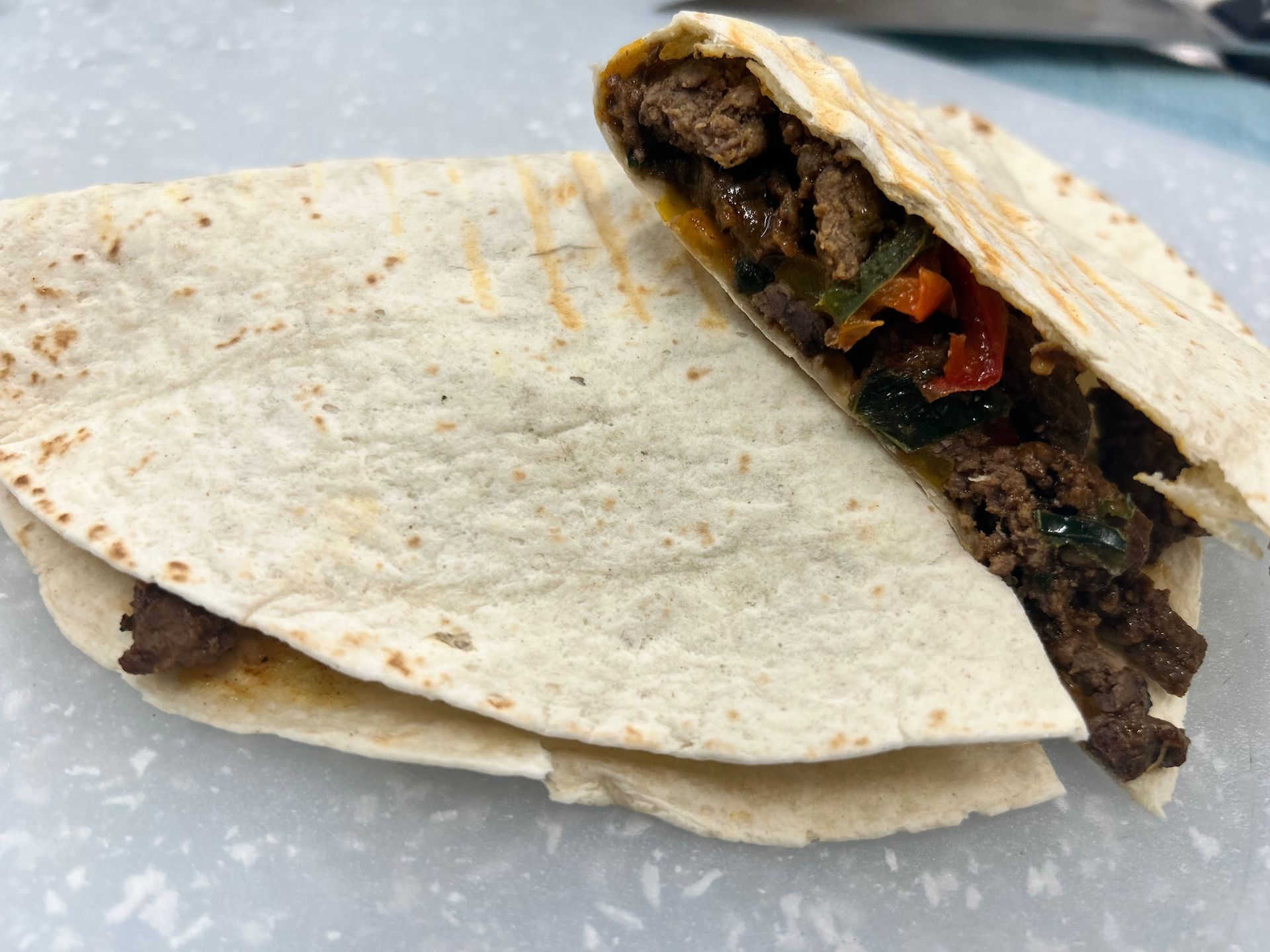 Beef and vegetable quesadilla, cut in half, on a surface.