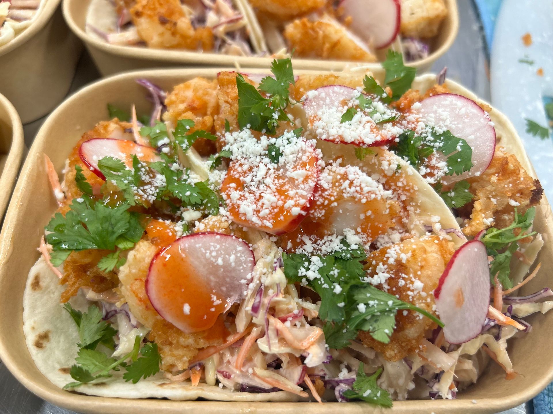 Shrimp tacos with slaw, radishes, cilantro, and cheese in a food container.