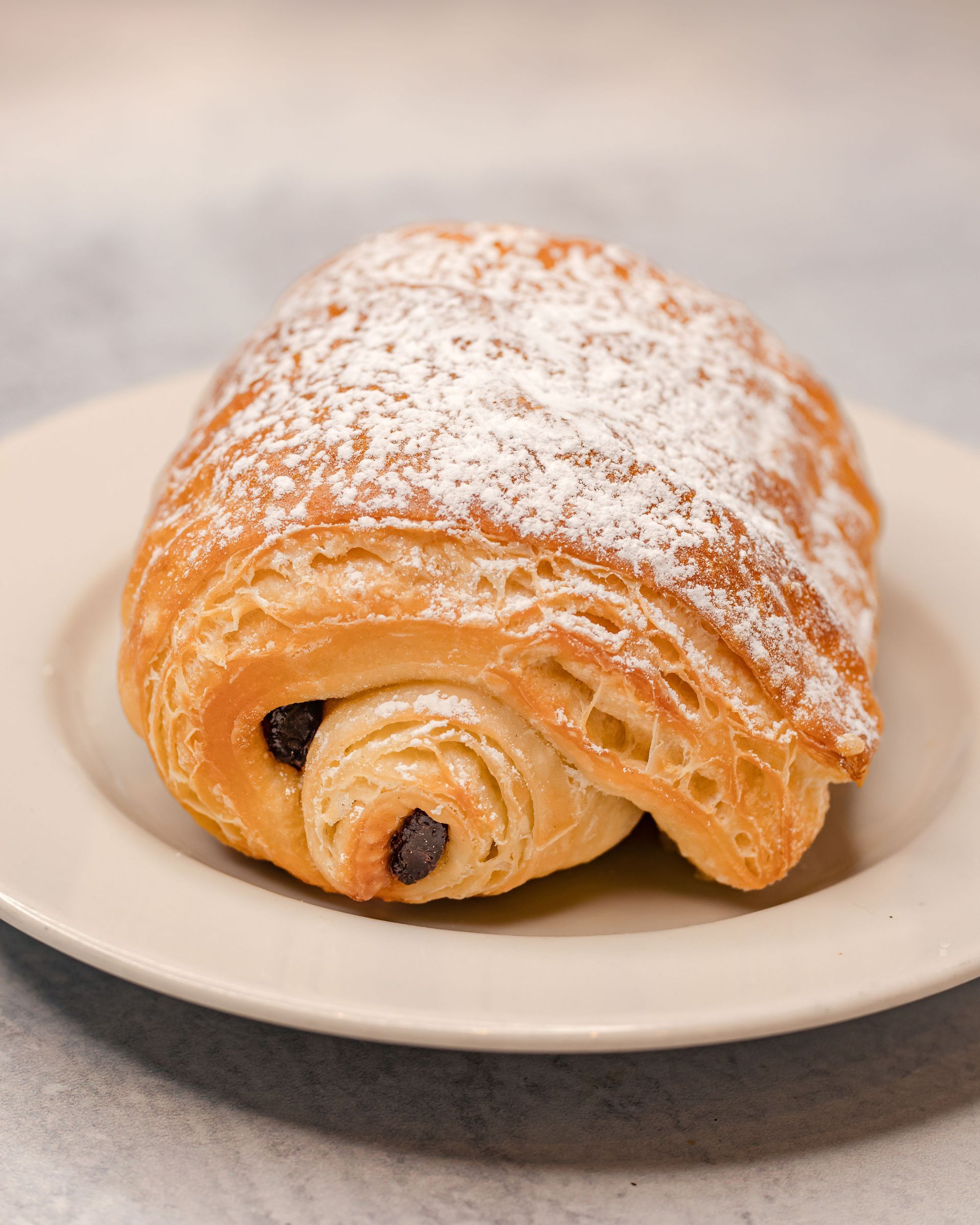 Pain au chocolat on a beige plate, dusted with powdered sugar.