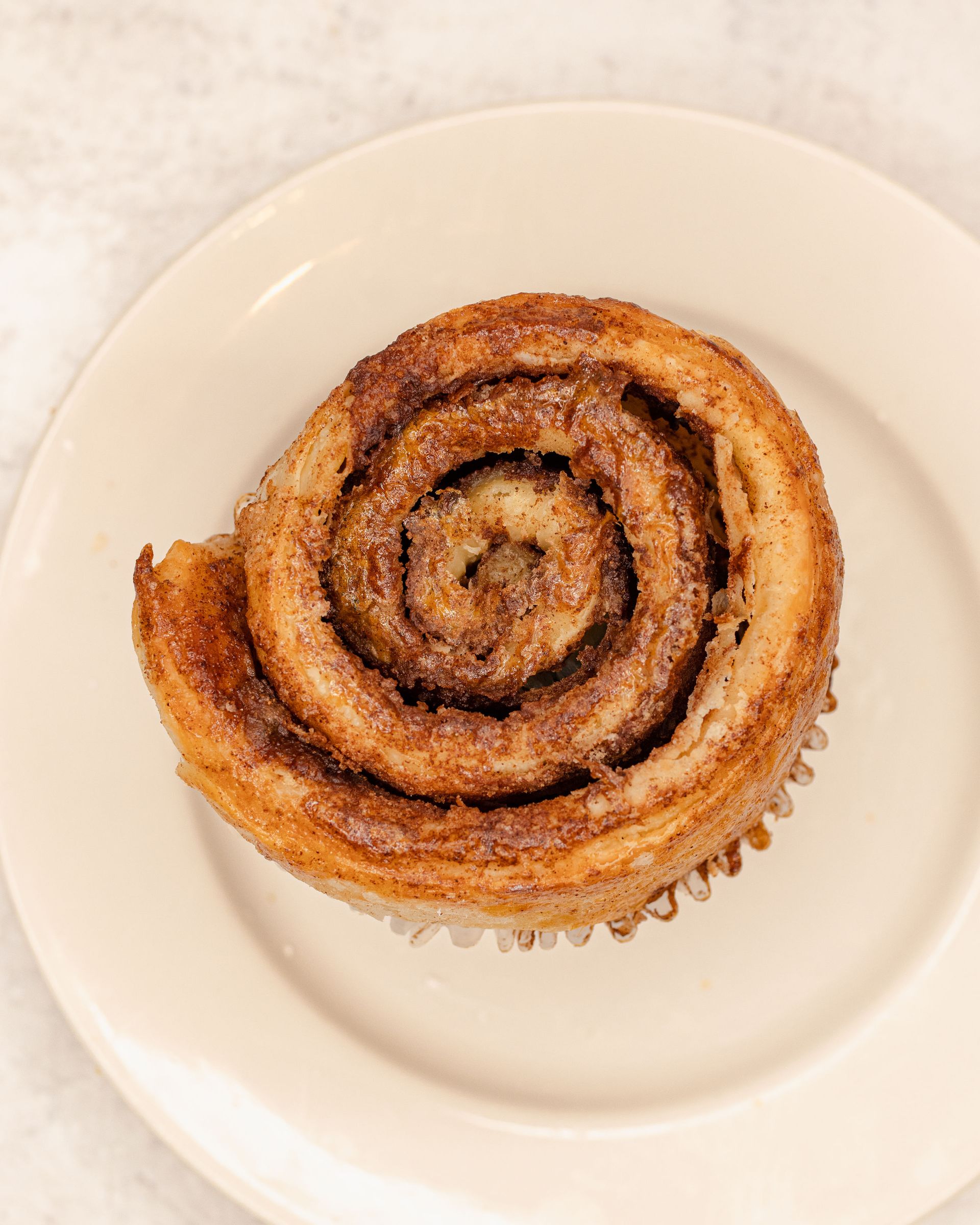 Cinnamon roll on a white plate, with visible swirls and baked golden-brown crust.