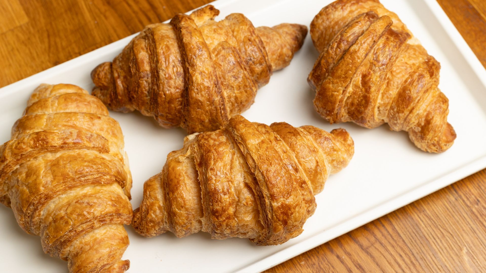 Golden-brown croissants arranged on a white rectangular plate, on a wooden table.