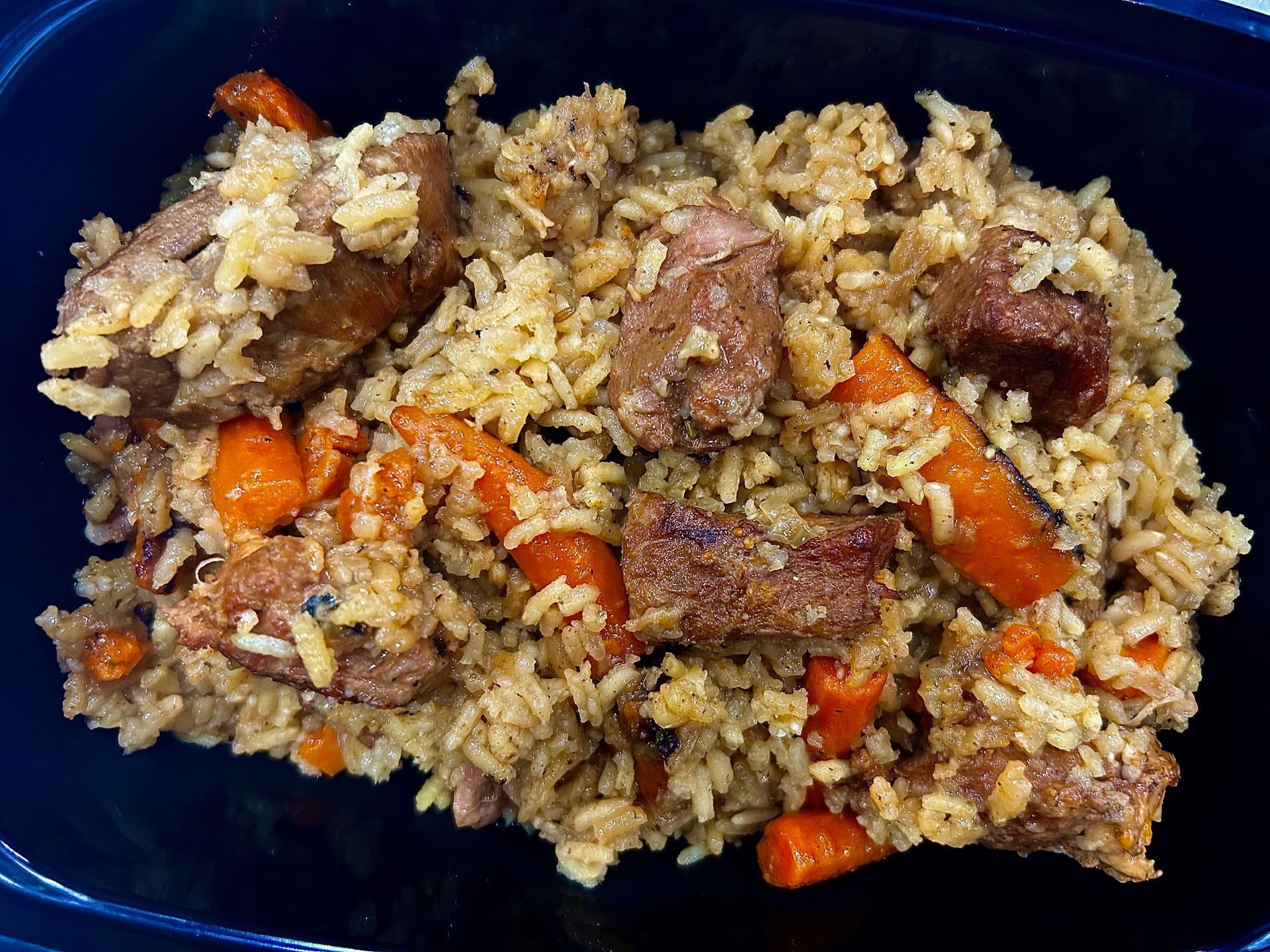 Pilaf: Rice dish with chunks of meat and carrots, in a black container.
