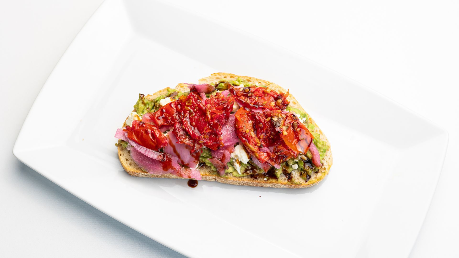 Toasted bread topped with pesto, pickled red onions, and roasted tomatoes on a white plate.