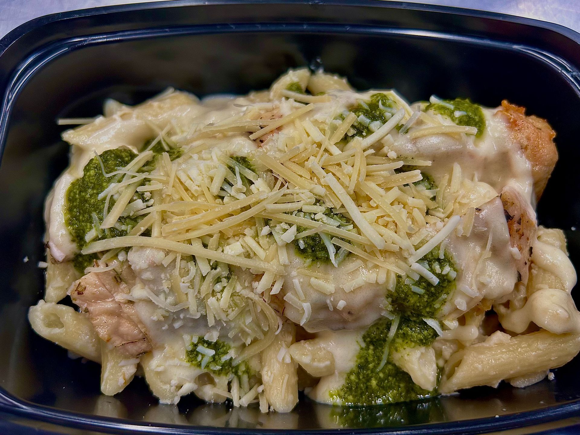 Pasta bake with pesto, cheese, and chicken in a black container.