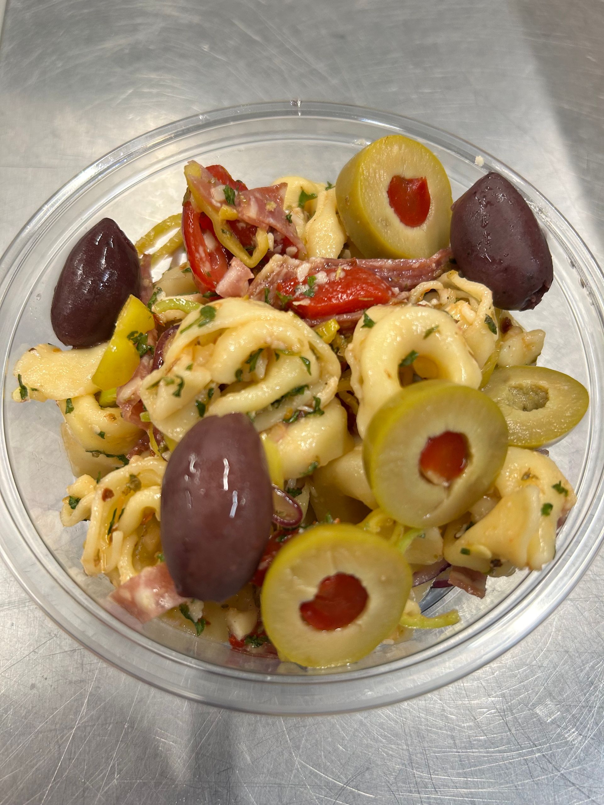 Tortellini salad in a clear bowl with olives, tomatoes, and herbs.