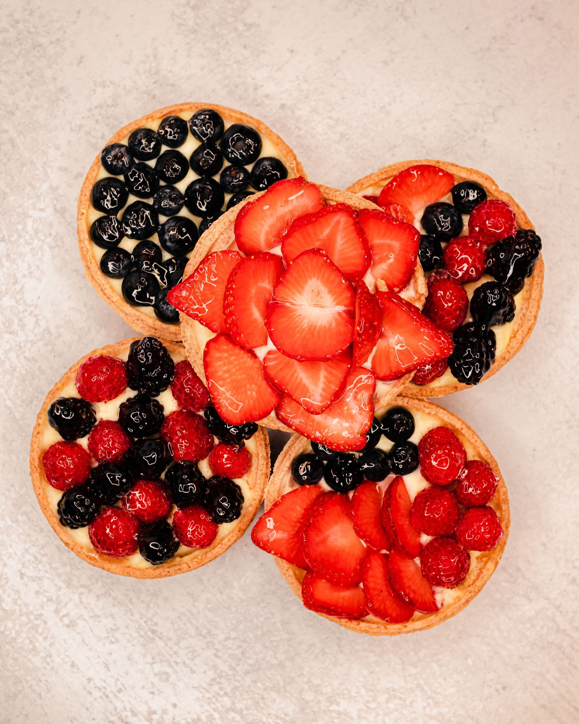 Fruit tarts with strawberries, blueberries, and raspberries arranged on a surface.