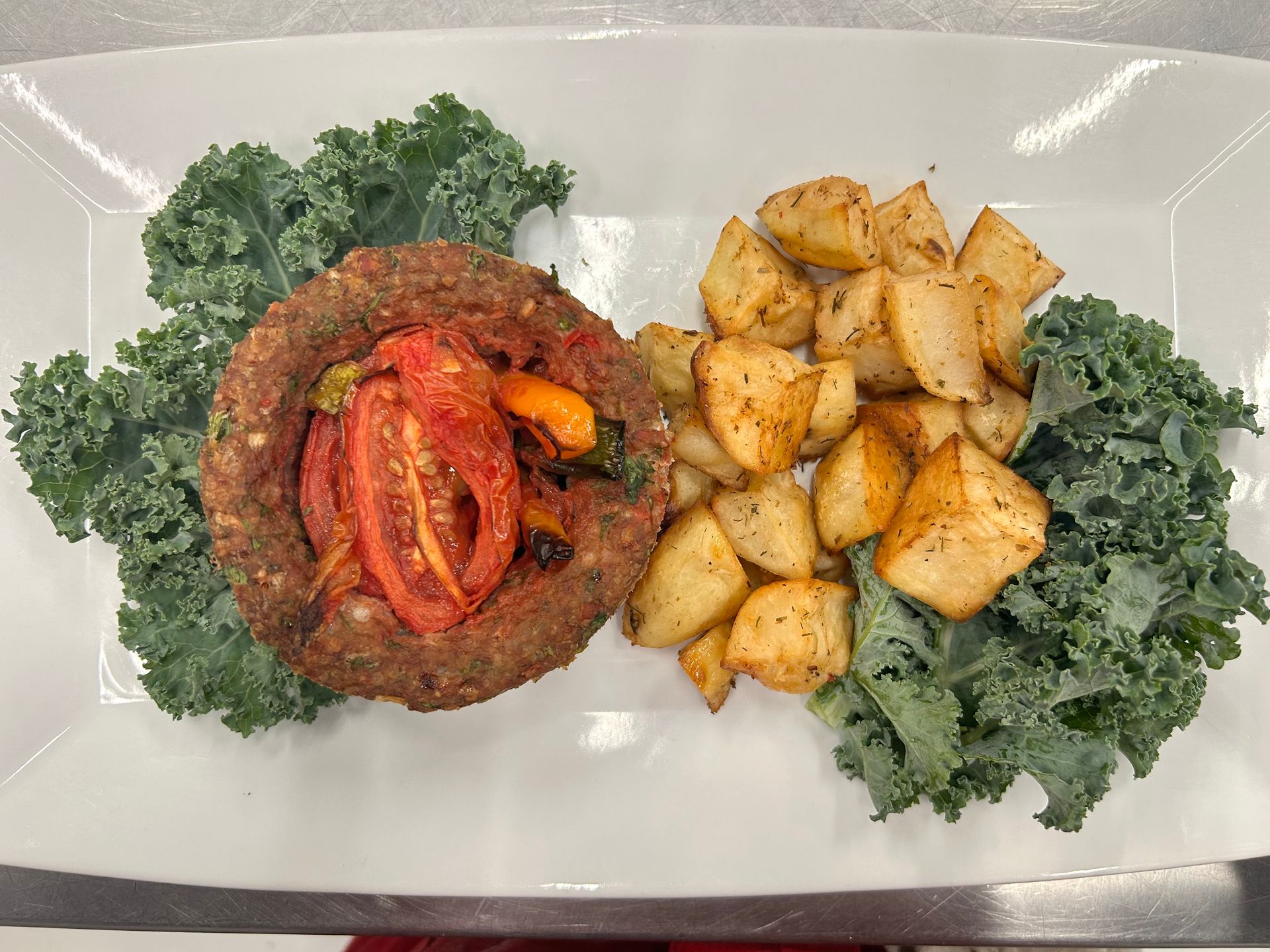 A ring-shaped meatloaf filled with vegetables, roasted potatoes, and kale on a white plate.