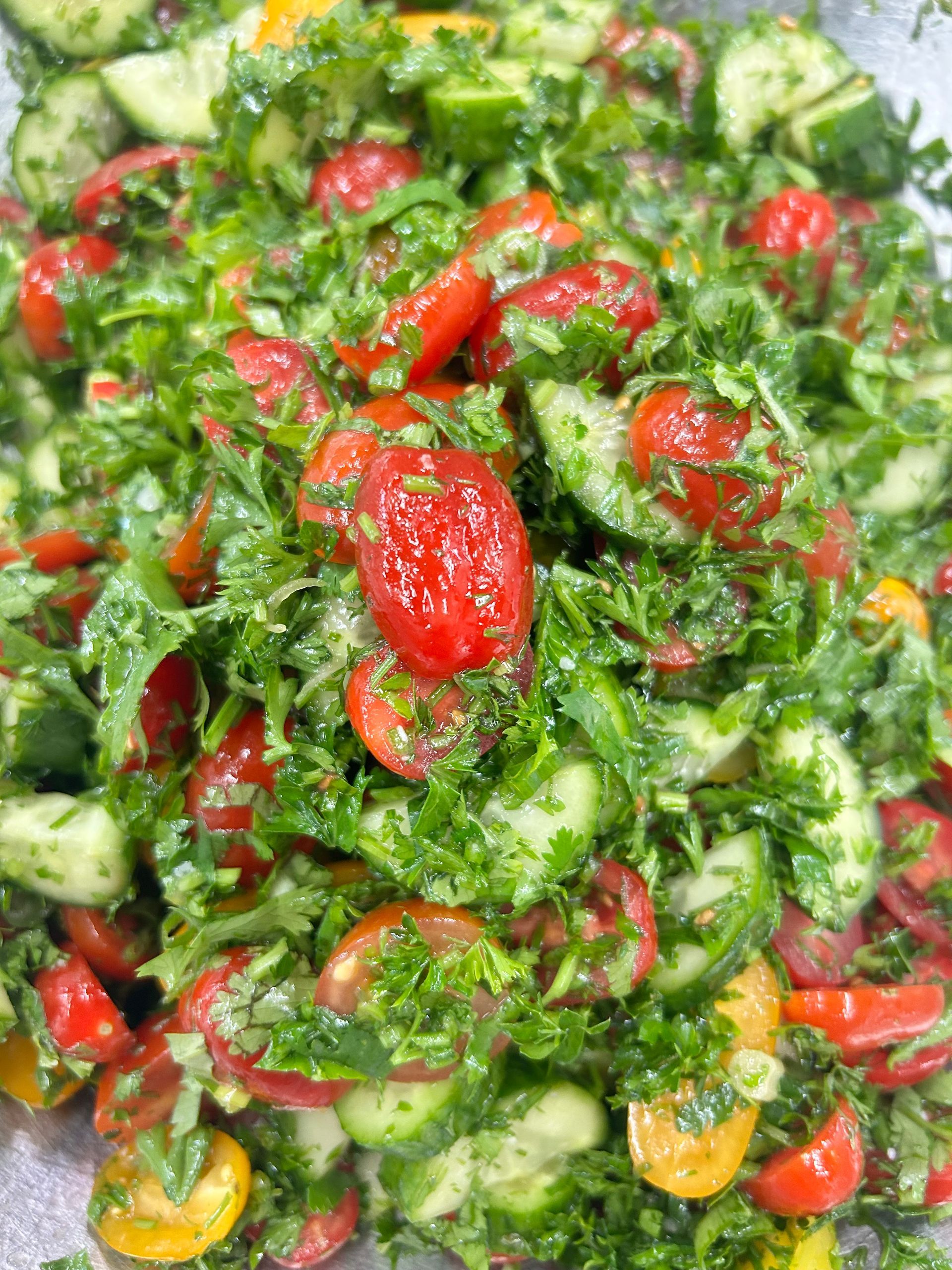 Salad with sliced cucumbers, tomatoes, and herbs, tossed in a green dressing.