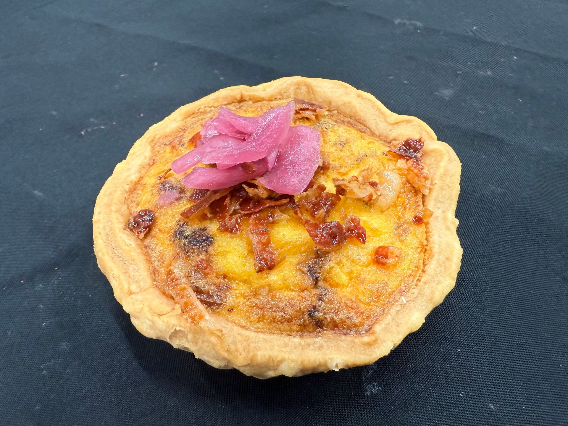 Savory quiche topped with pink pickled onions on a dark surface.