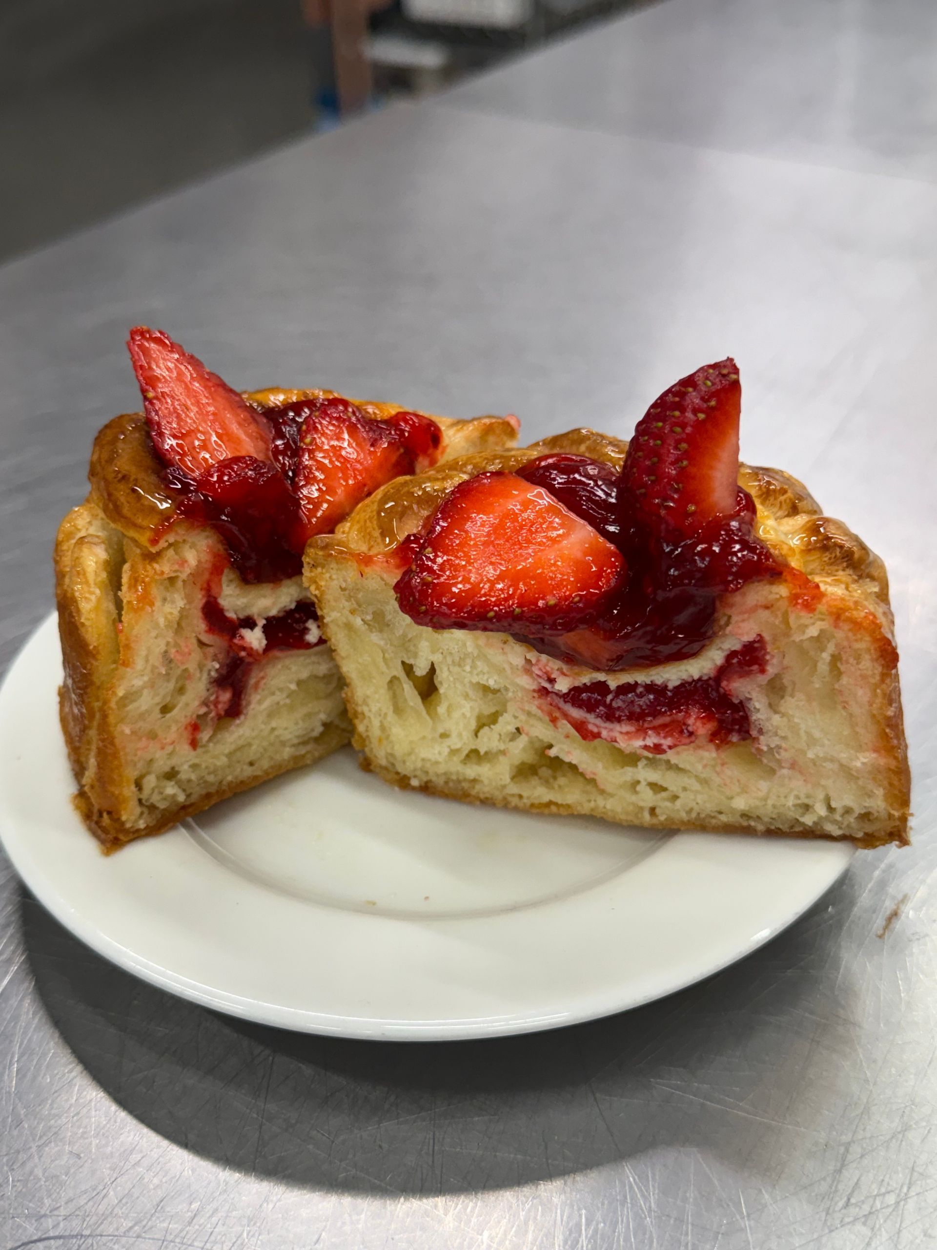 Strawberry danish pastry on a white plate, cut in half to show layers and filling. Red strawberries are on top.