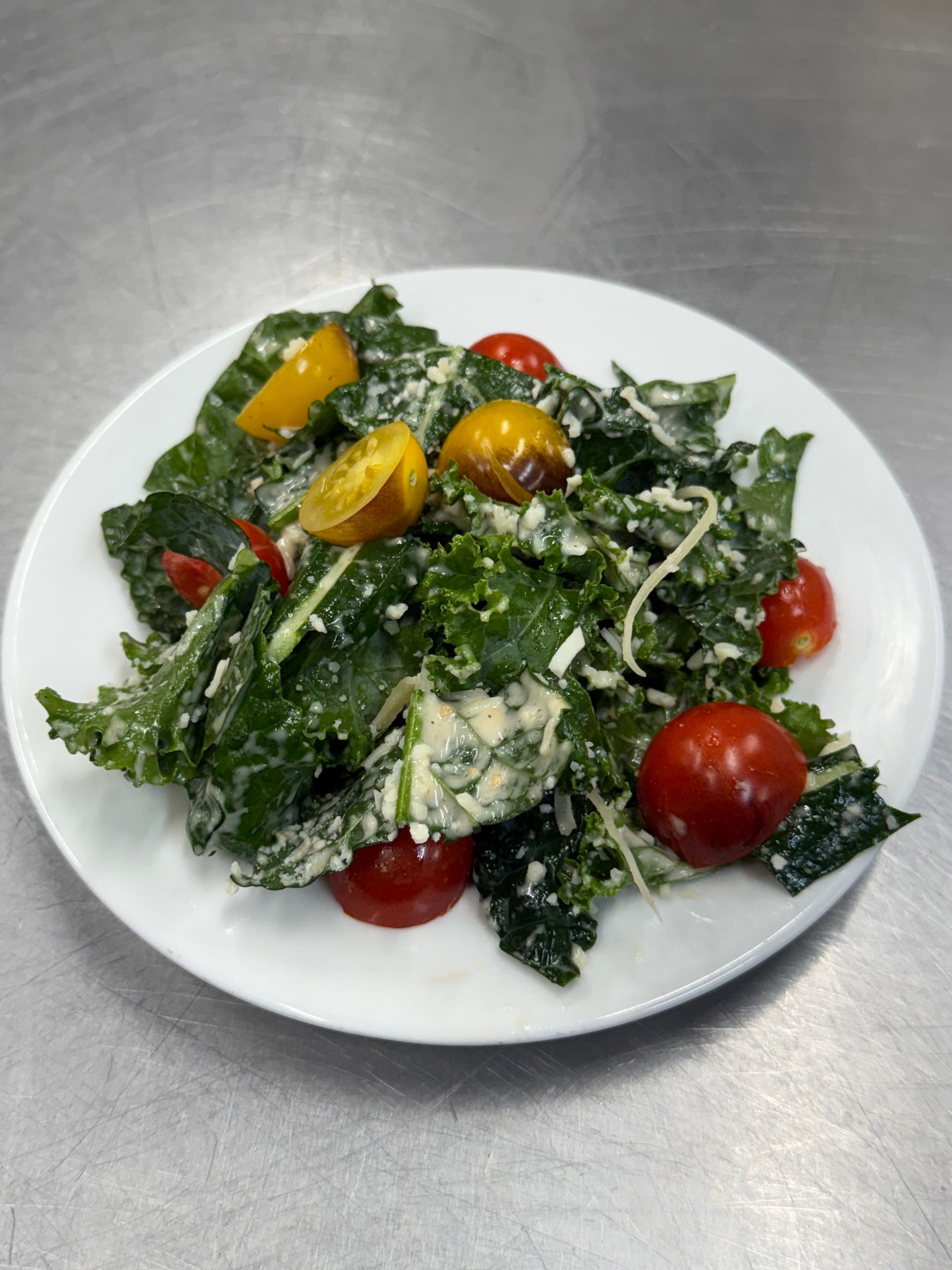 Salad with kale, cherry tomatoes, and dressing on a white plate.