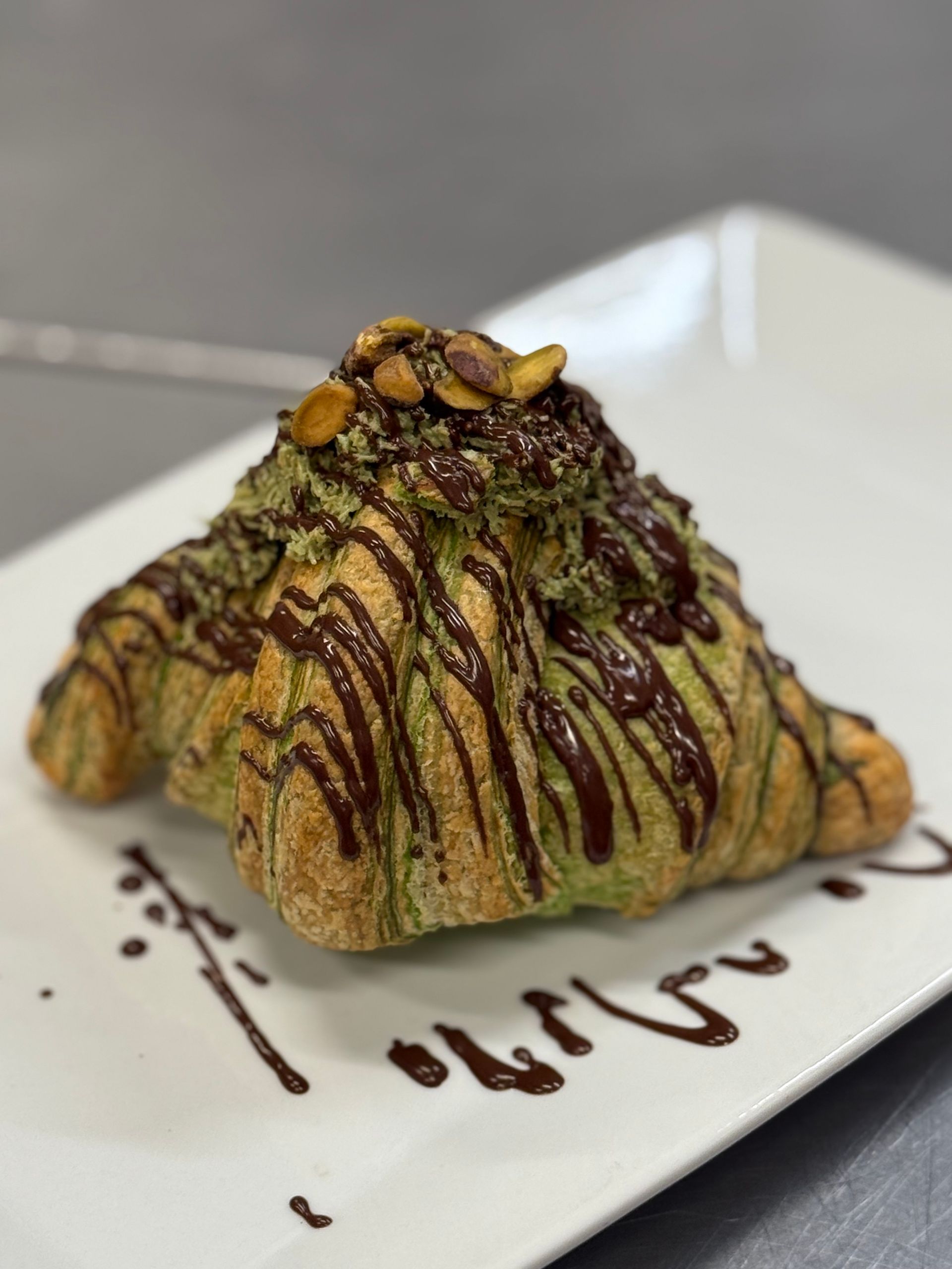 Croissant drizzled with chocolate and green matcha, topped with nuts, on a white plate.