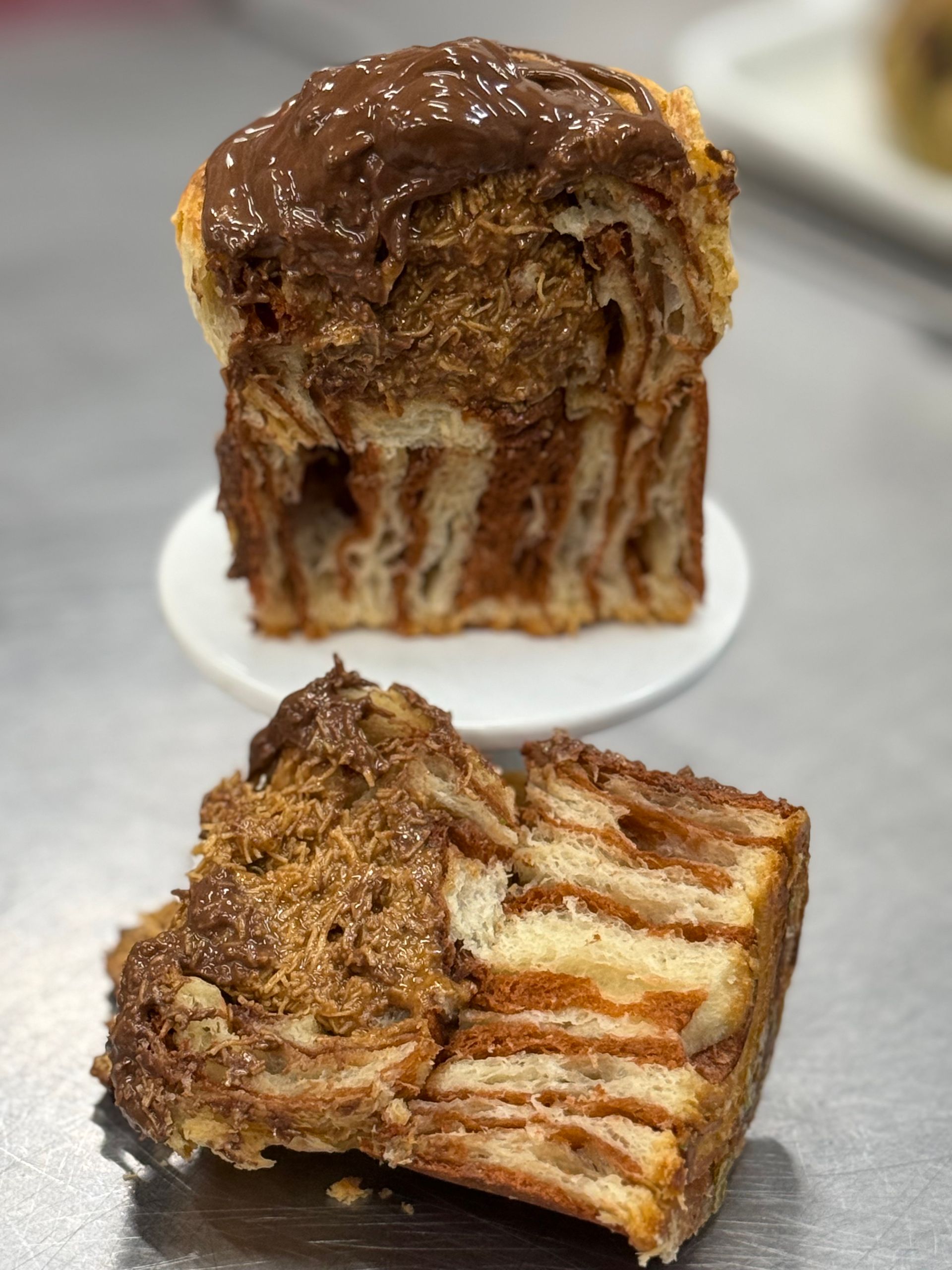 Chocolate babka cut in half, showcasing layers of dough and chocolate, on a white plate and surface.