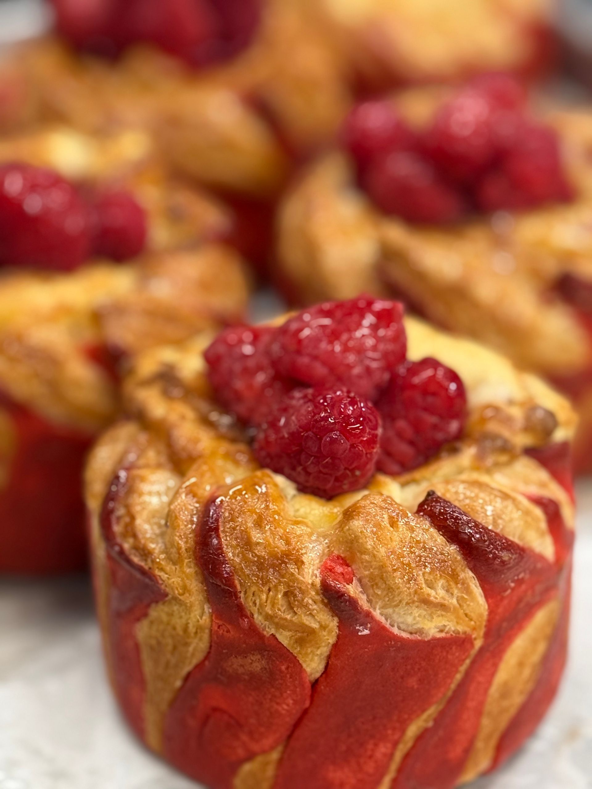 Close-up of baked pastry with raspberry topping; red and golden-brown layers.