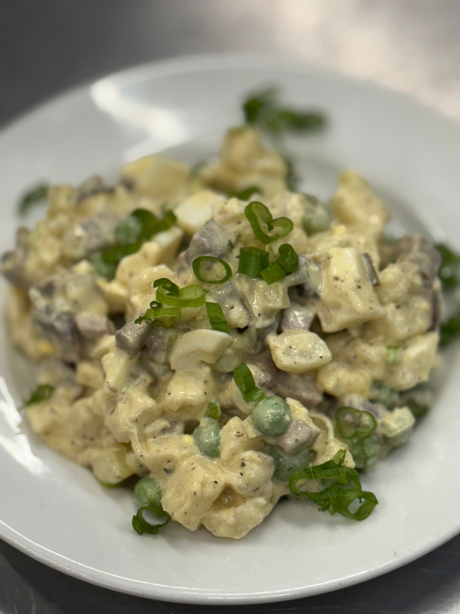 Potato salad with eggs, peas, and green onions on a white plate.