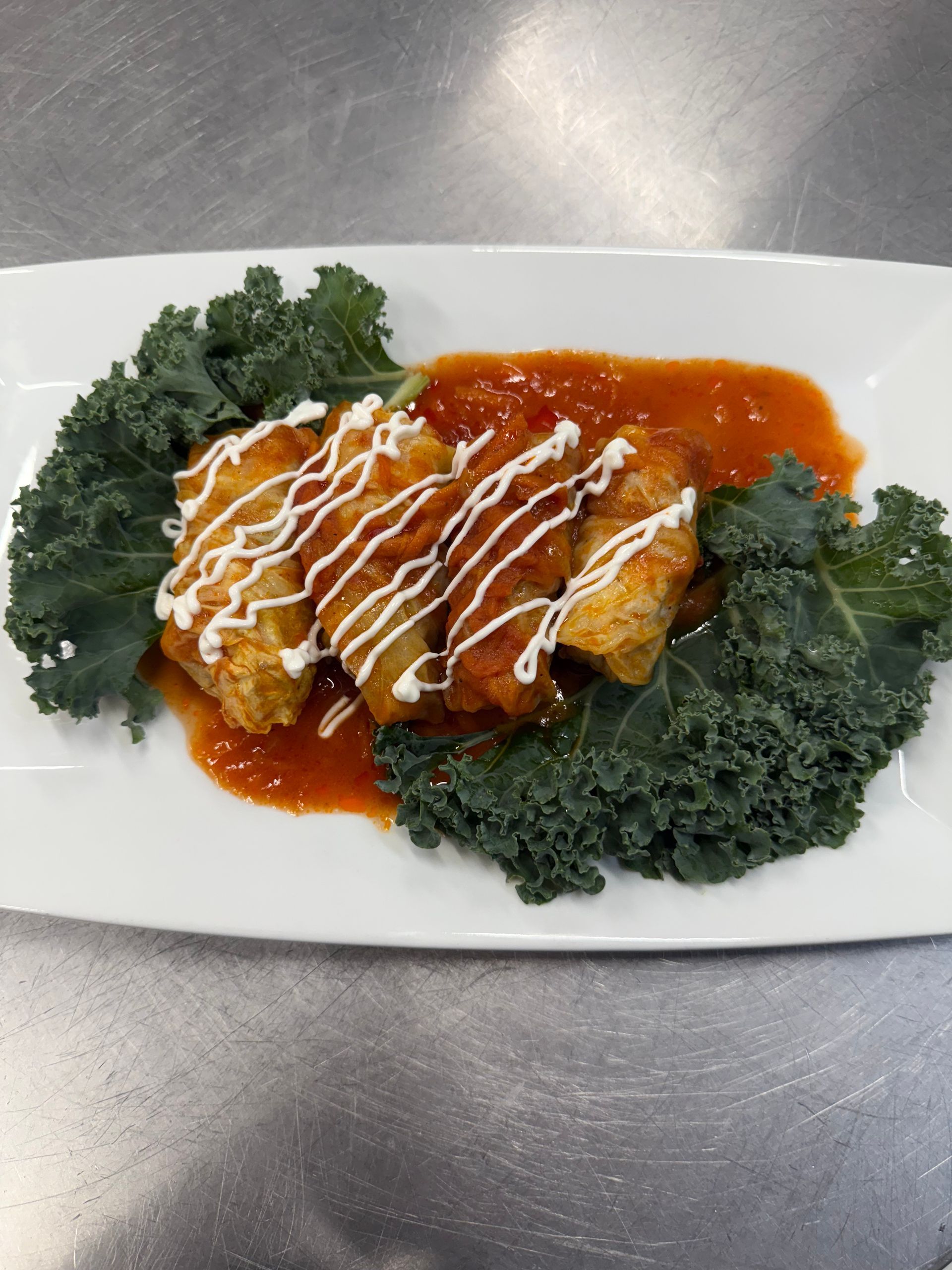 Fried food with tomato sauce and cream drizzle, garnished with kale on a white plate.