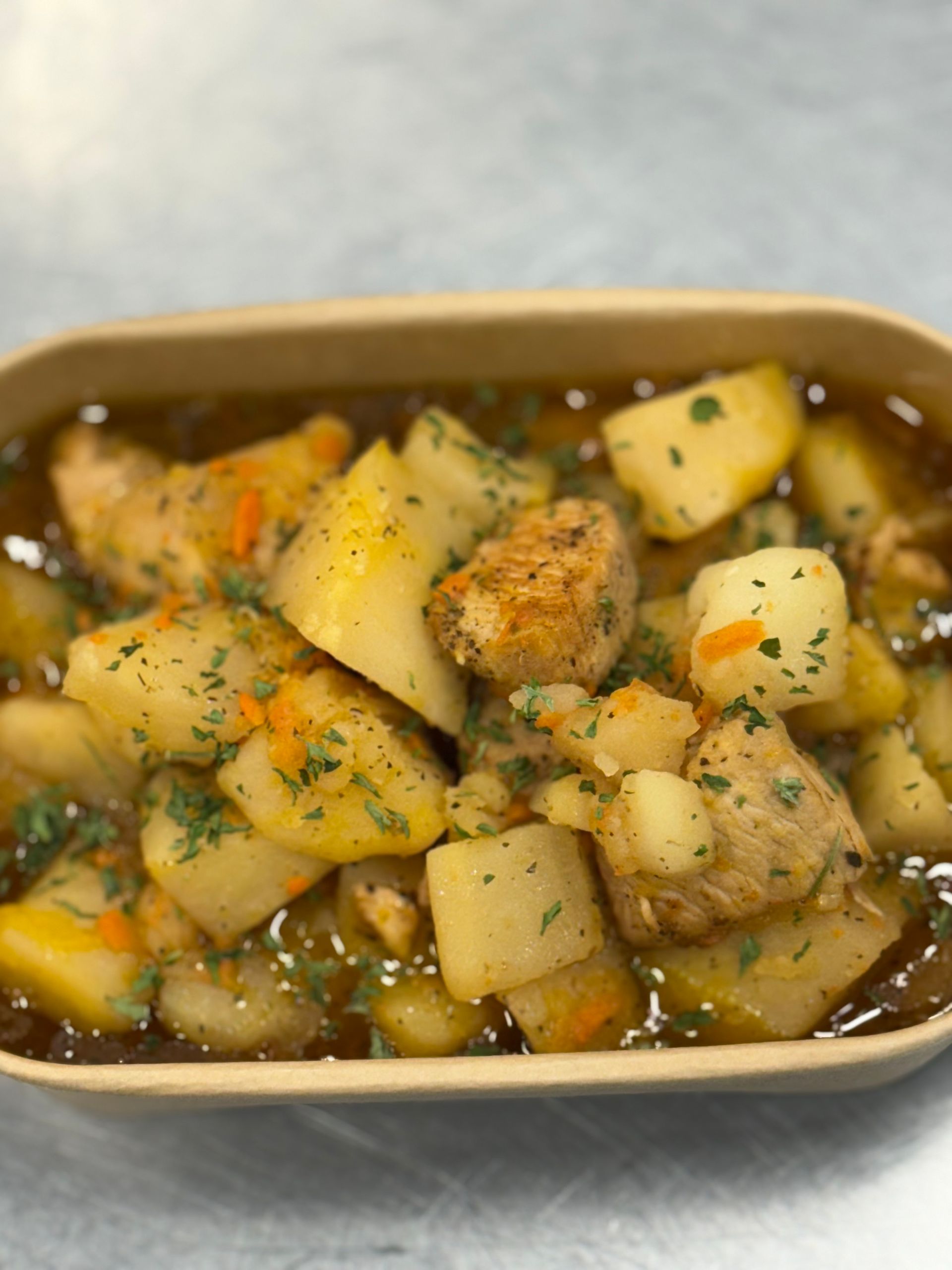 Stew with potatoes, carrots, and meat in a tan container, garnished with parsley.