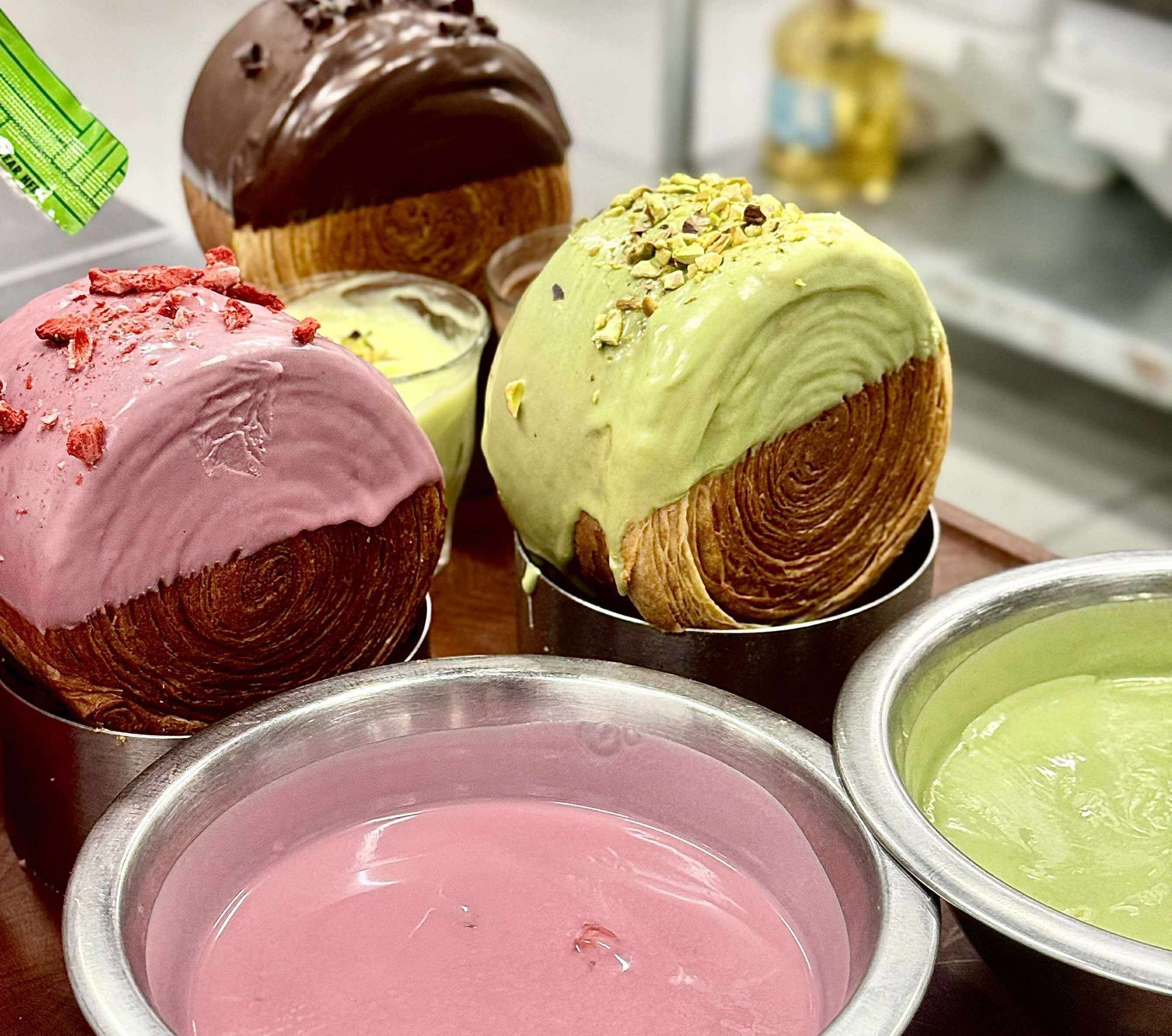 Close-up of four pastry desserts with colorful frosting and toppings, surrounded by small bowls of cream.