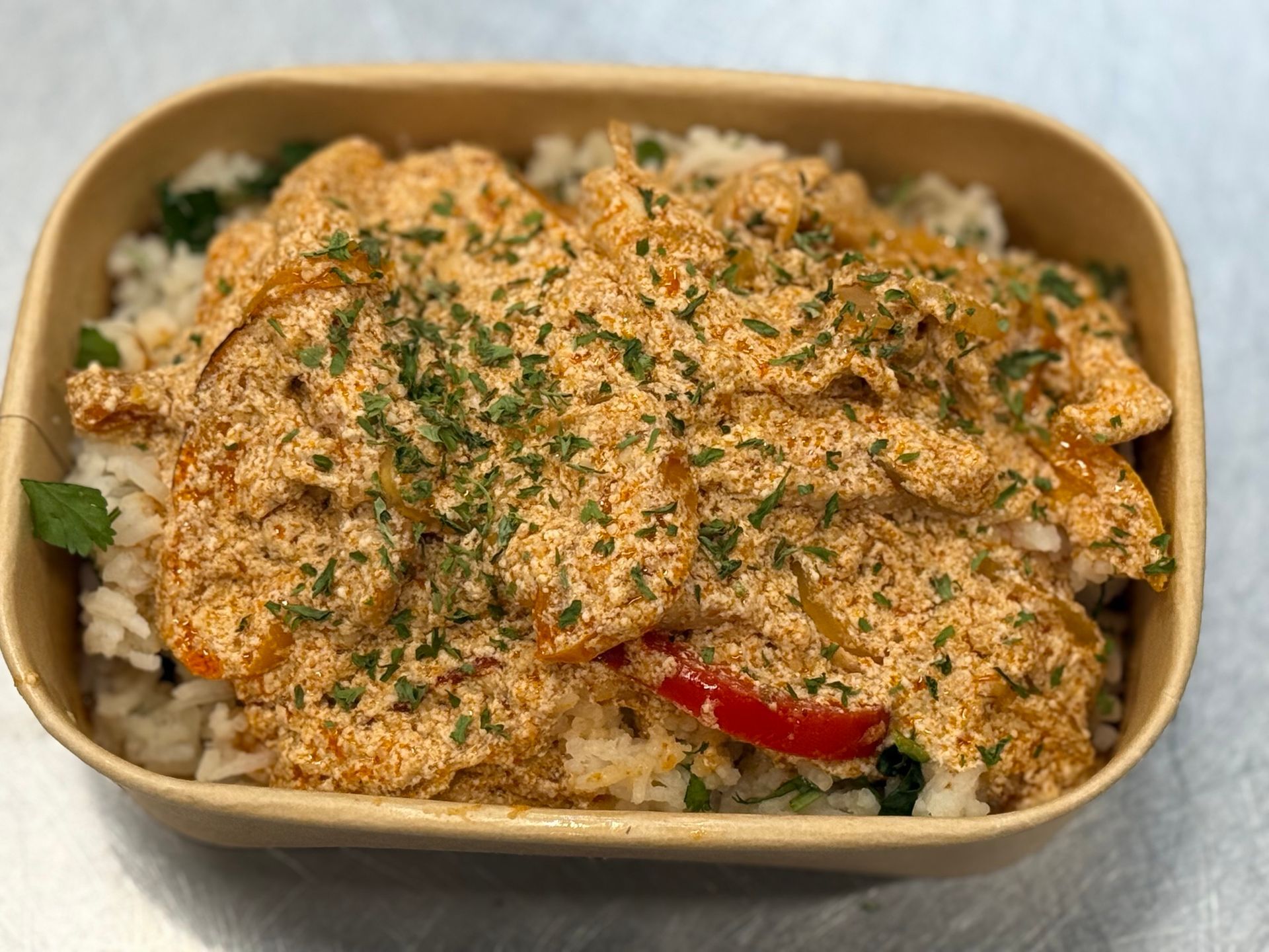 Rice bowl with creamy orange sauce, topped with parsley.