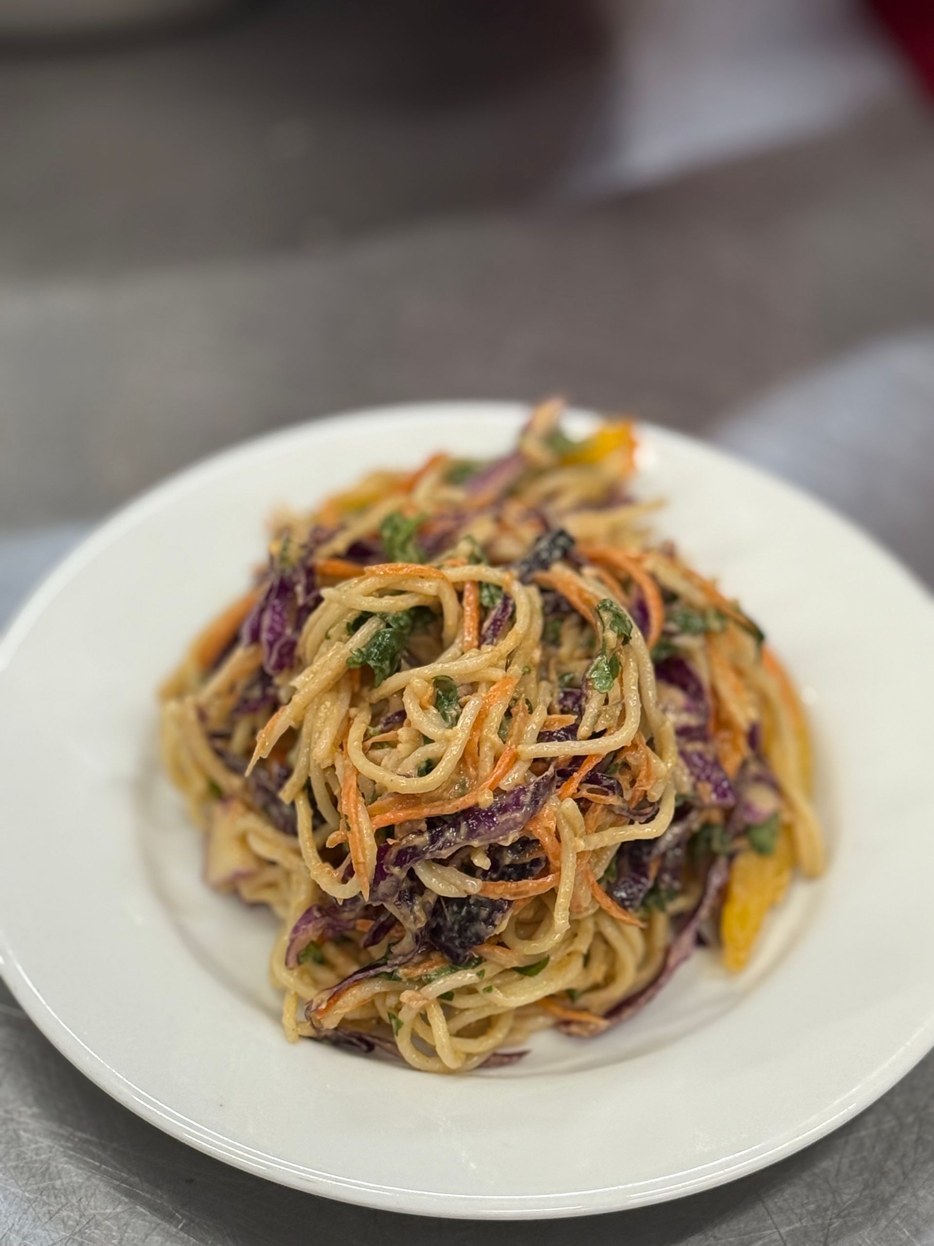 Spaghetti salad with shredded carrots, purple cabbage, and a creamy dressing on a white plate.