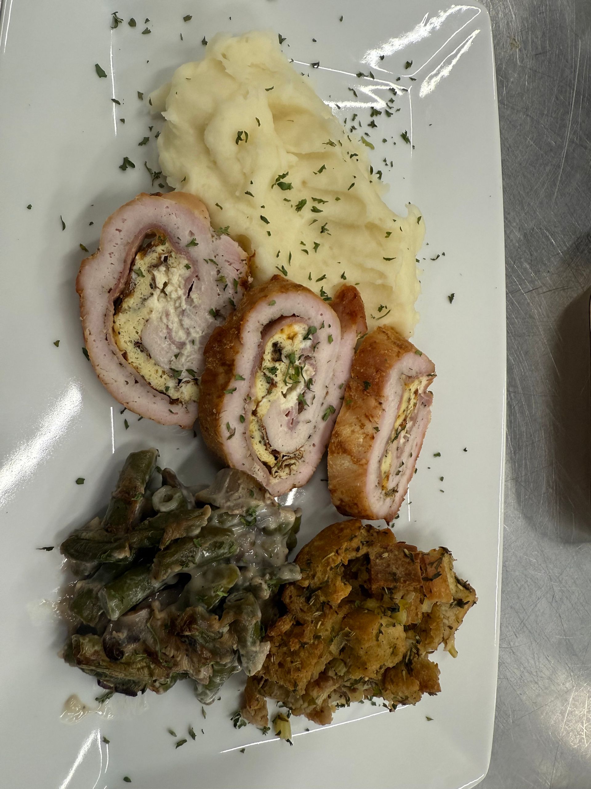Plate with sliced stuffed meat, mashed potatoes, green beans, and stuffing.