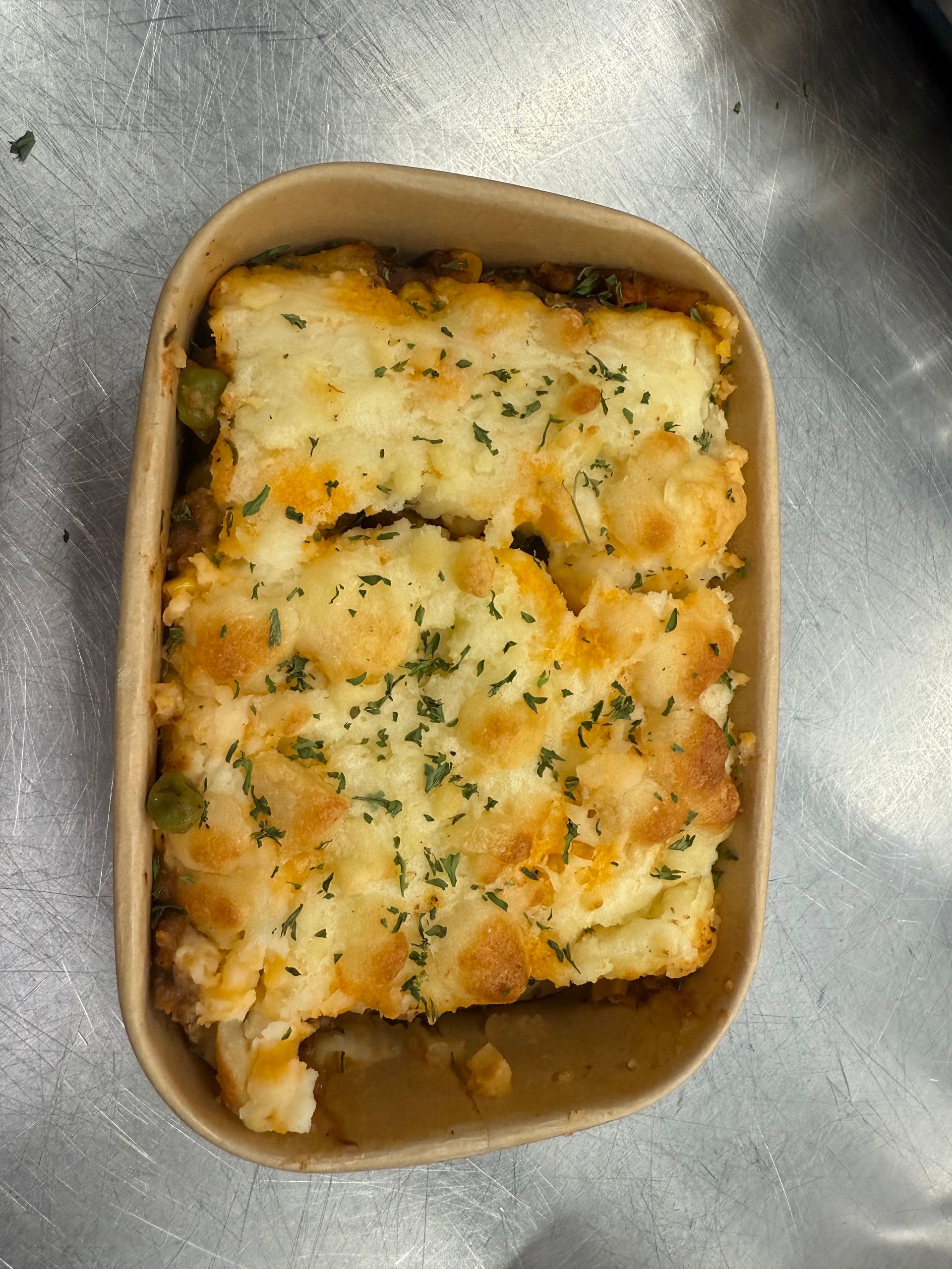 Casserole dish with mashed potato topping and garnish in a brown container.