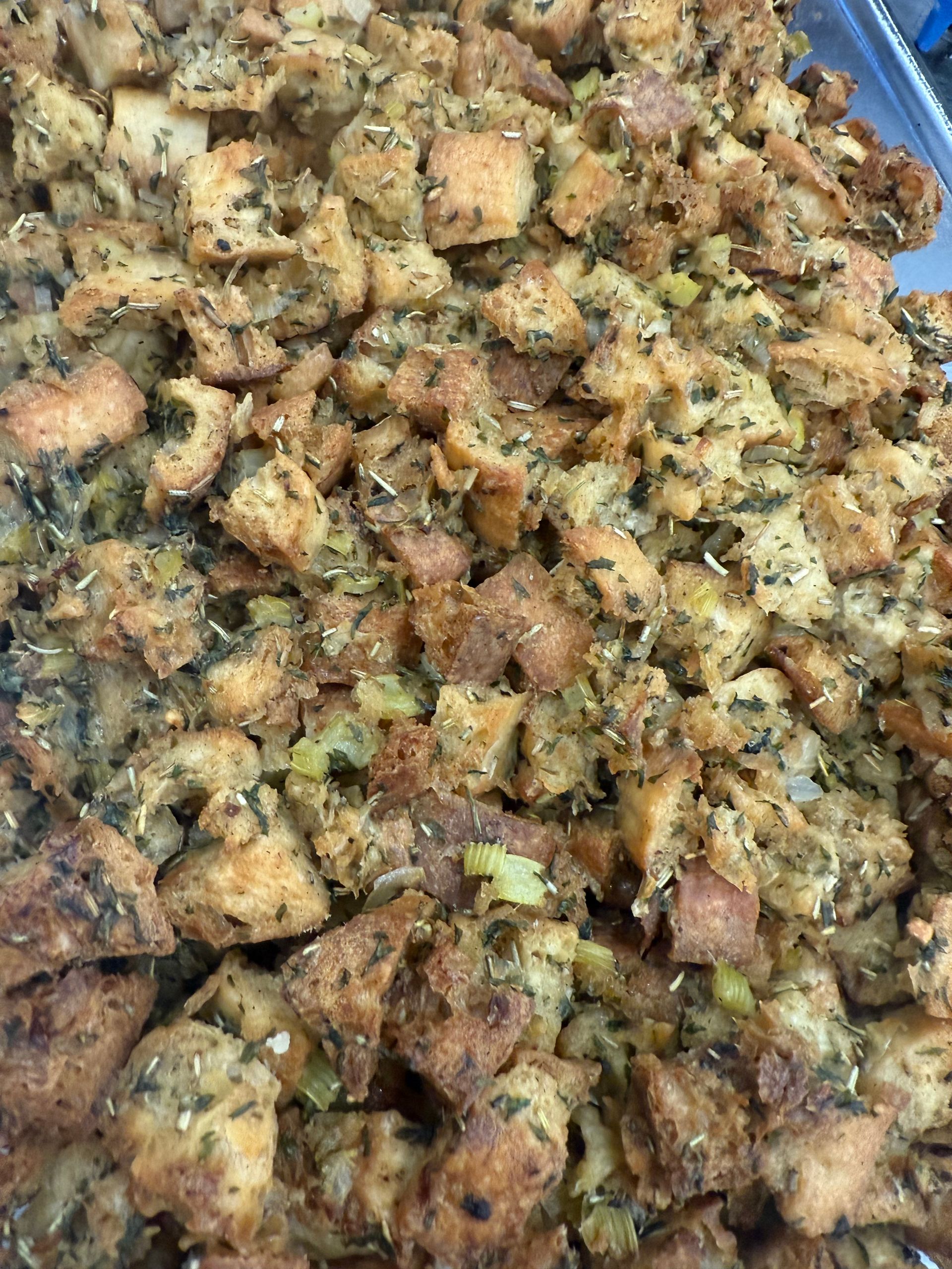 Close-up of a large dish of seasoned, baked stuffing with herbs and vegetables.