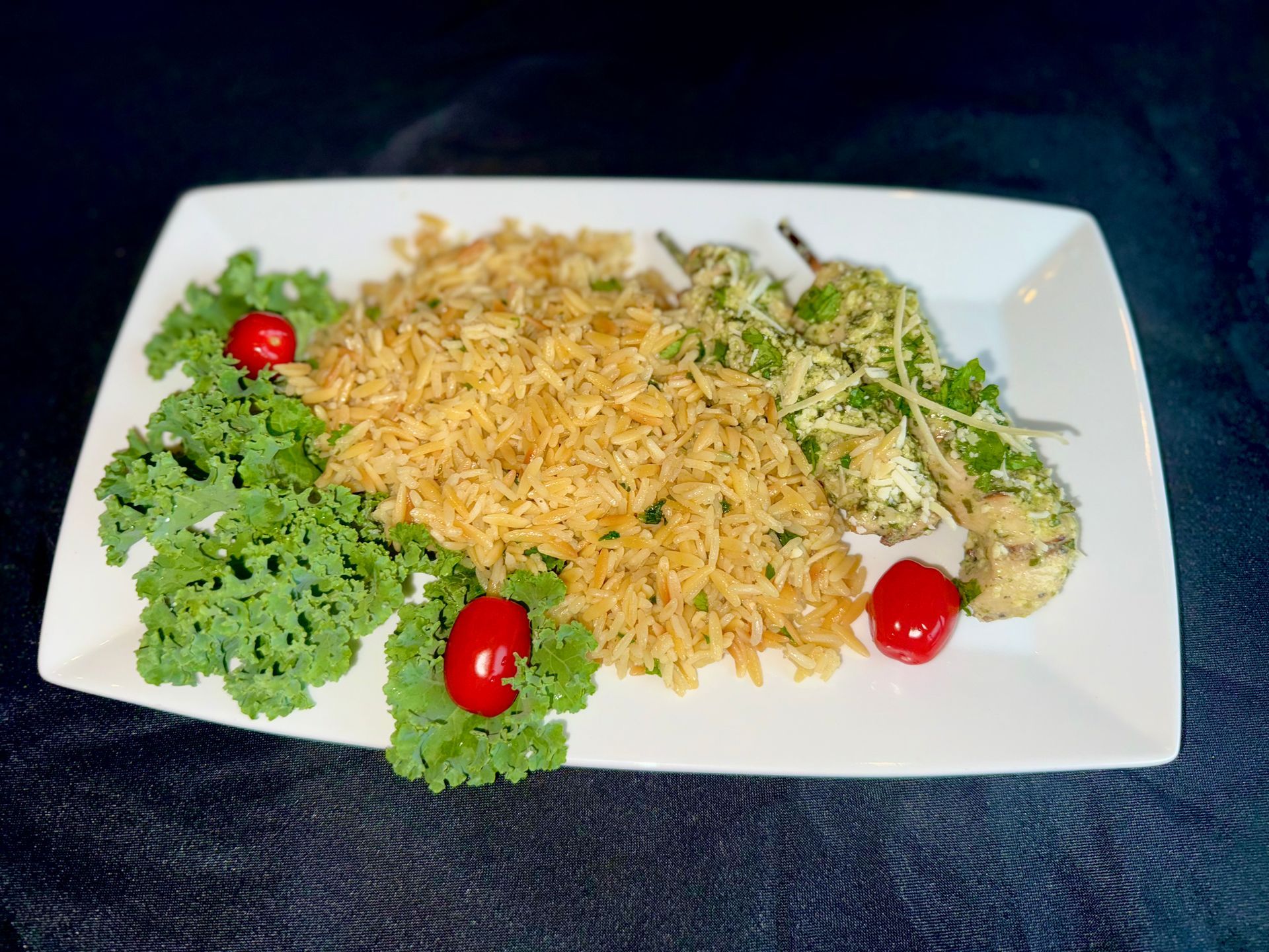 Rice dish with green vegetables, small red tomatoes, and garnish on a white plate.