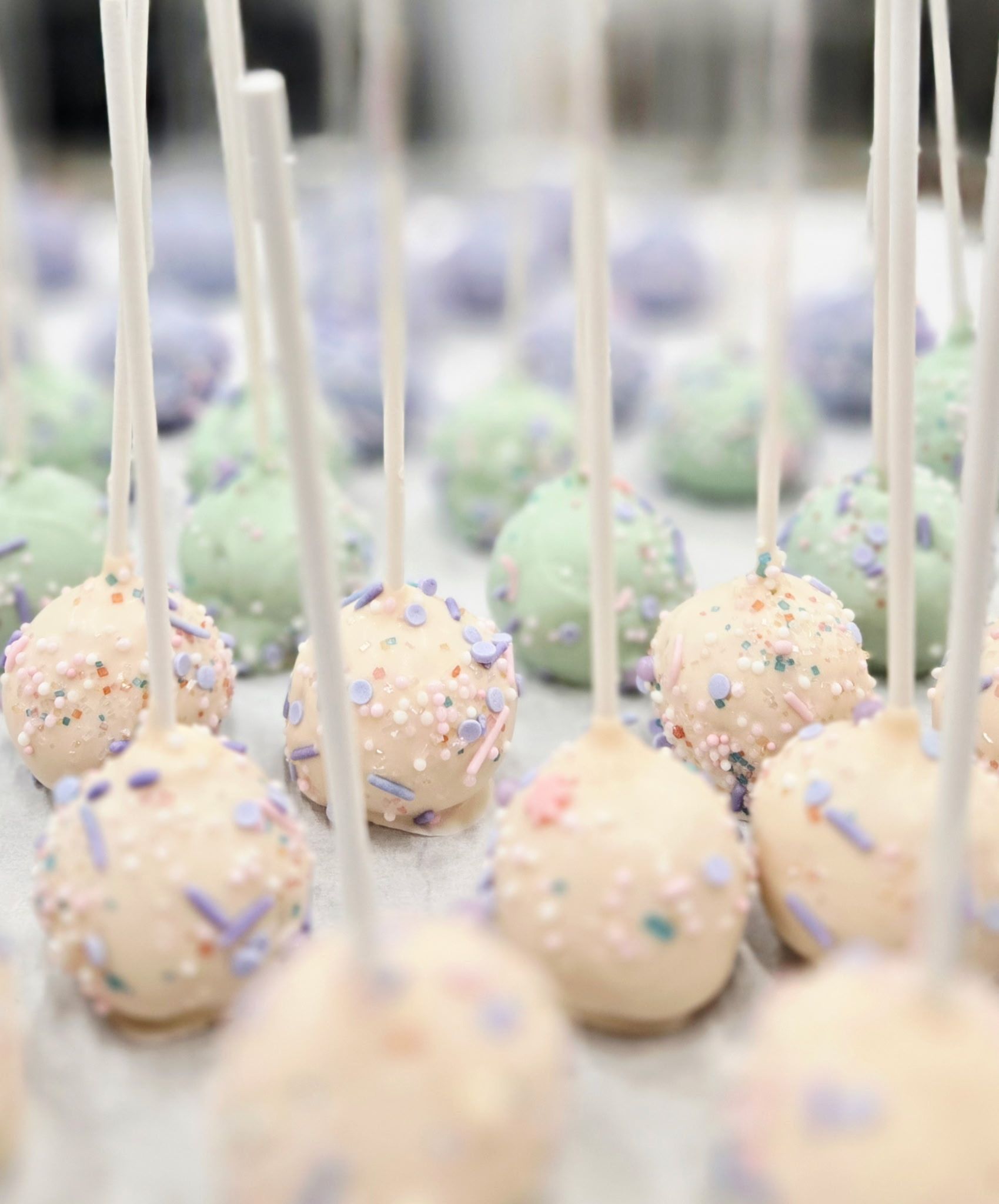 Cake pops in various pastel colors with sprinkles on sticks.