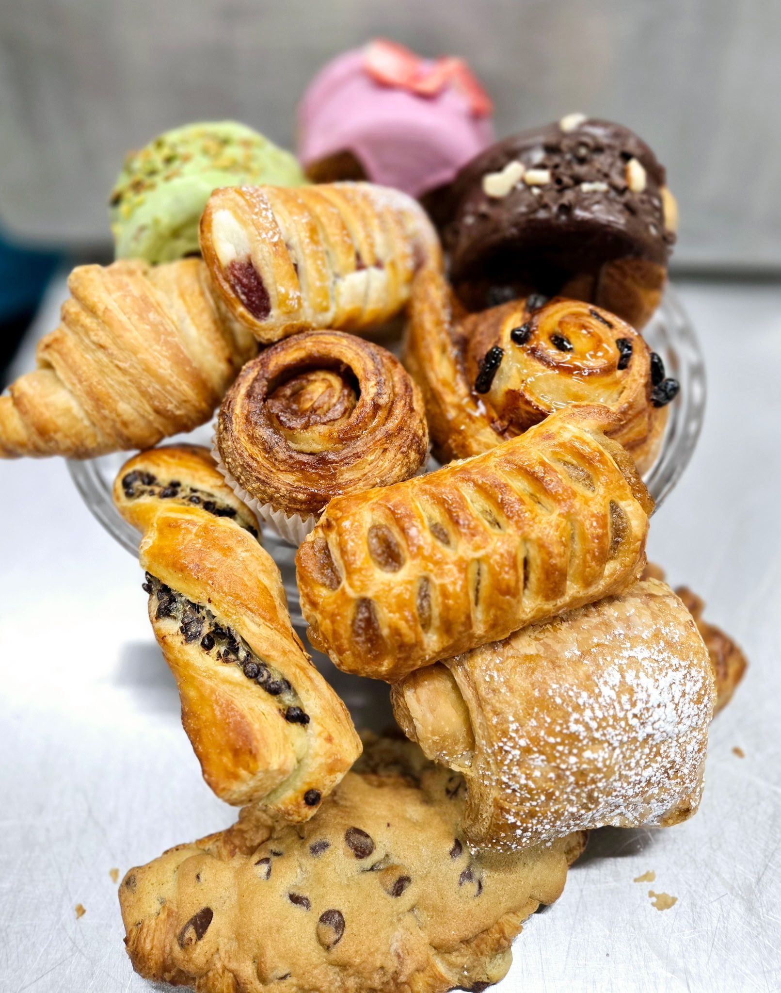 Assorted pastries, including croissants, danishes, and muffins, arranged in a glass bowl.