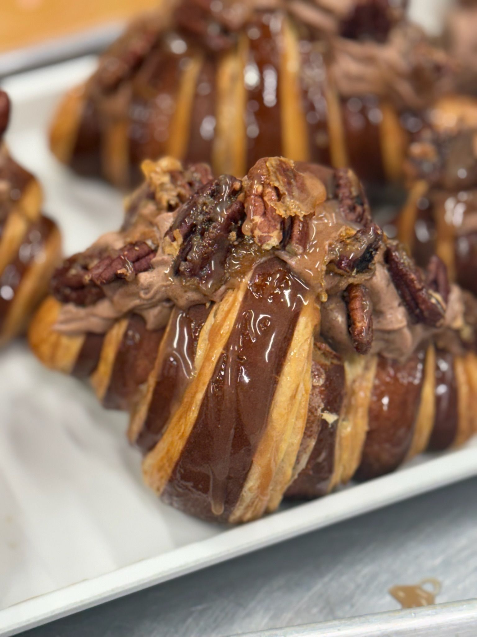 Chocolate croissant pastry topped with chocolate cream, pecans, and glaze on a white tray.