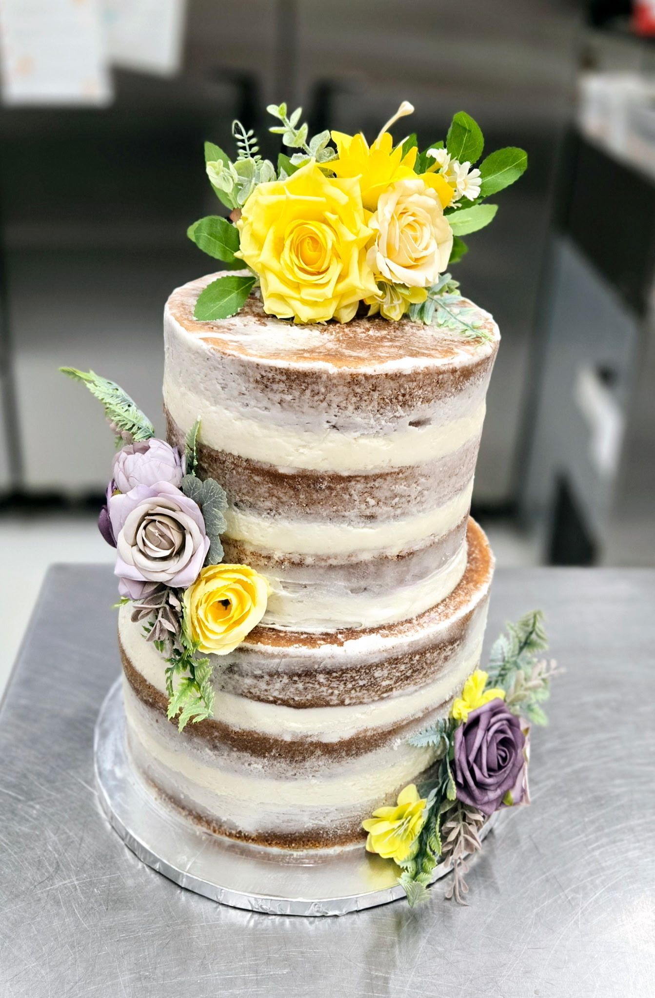 Two-tiered naked cake decorated with yellow and purple flowers and greenery.