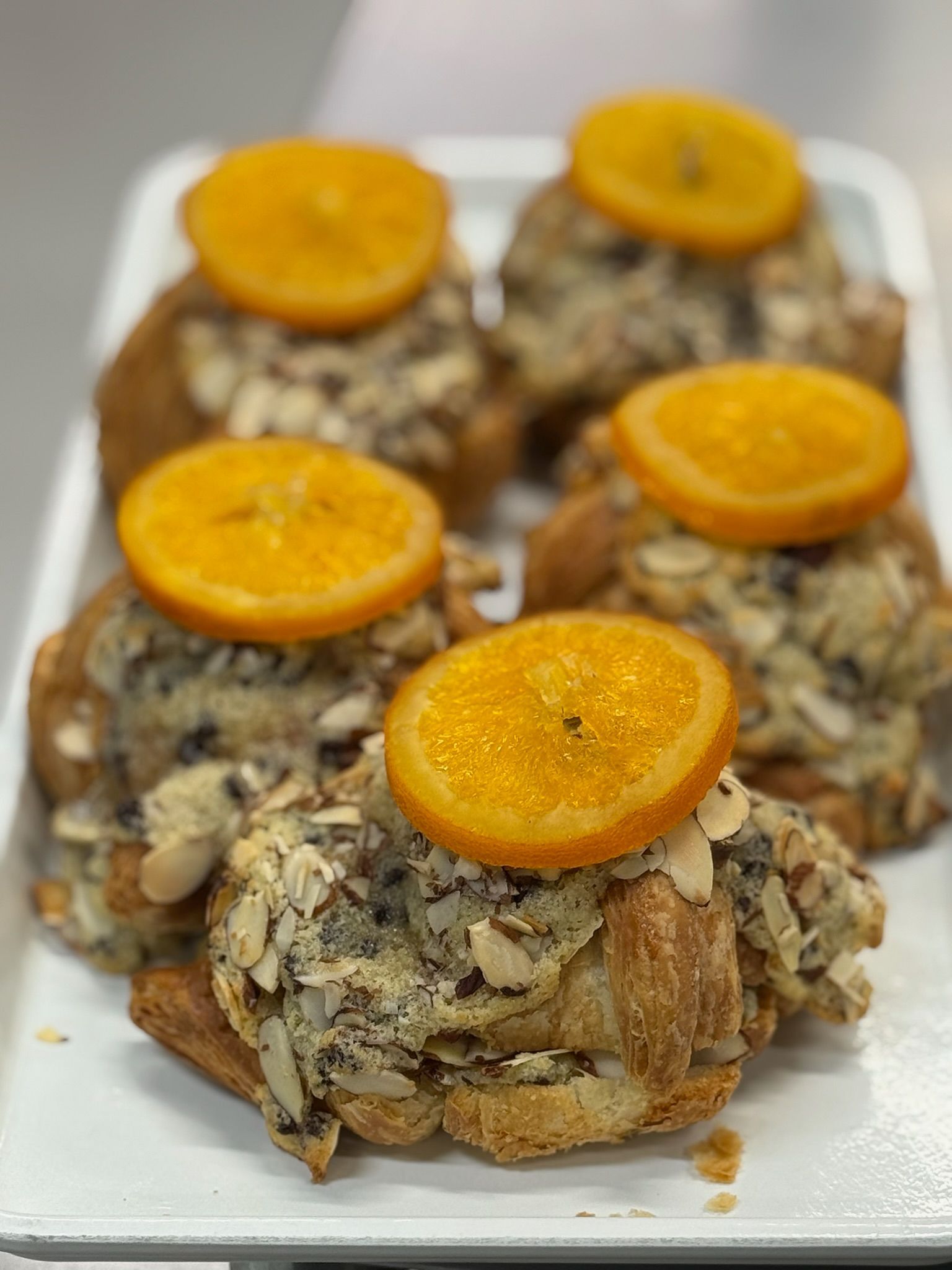 Croissants topped with almond flakes, cream, and orange slices on a white tray.