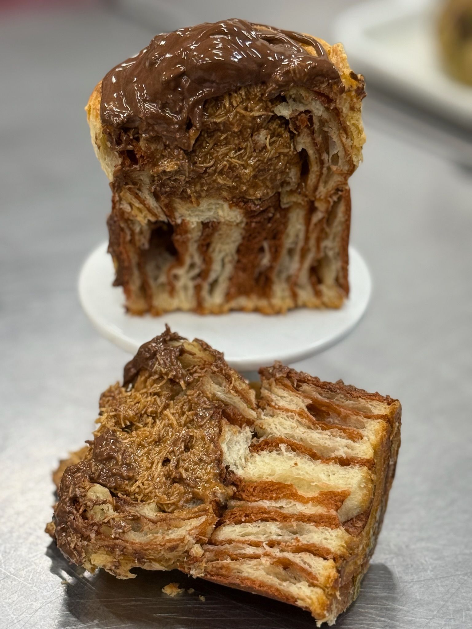 Sliced chocolate babka on a white plate, showing layered dough with chocolate swirls and topping.