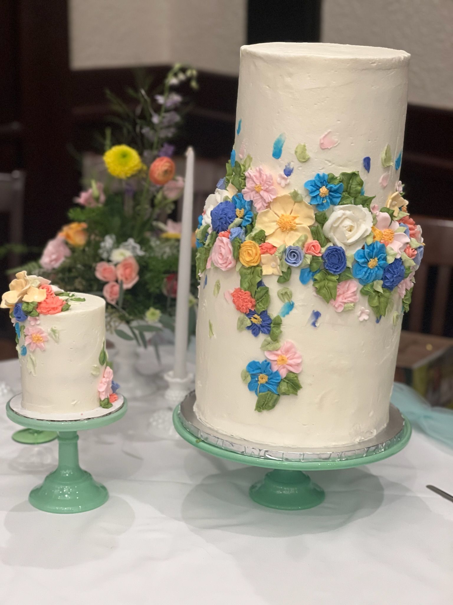 Two tiered cakes decorated with buttercream flowers, on green cake stands.
