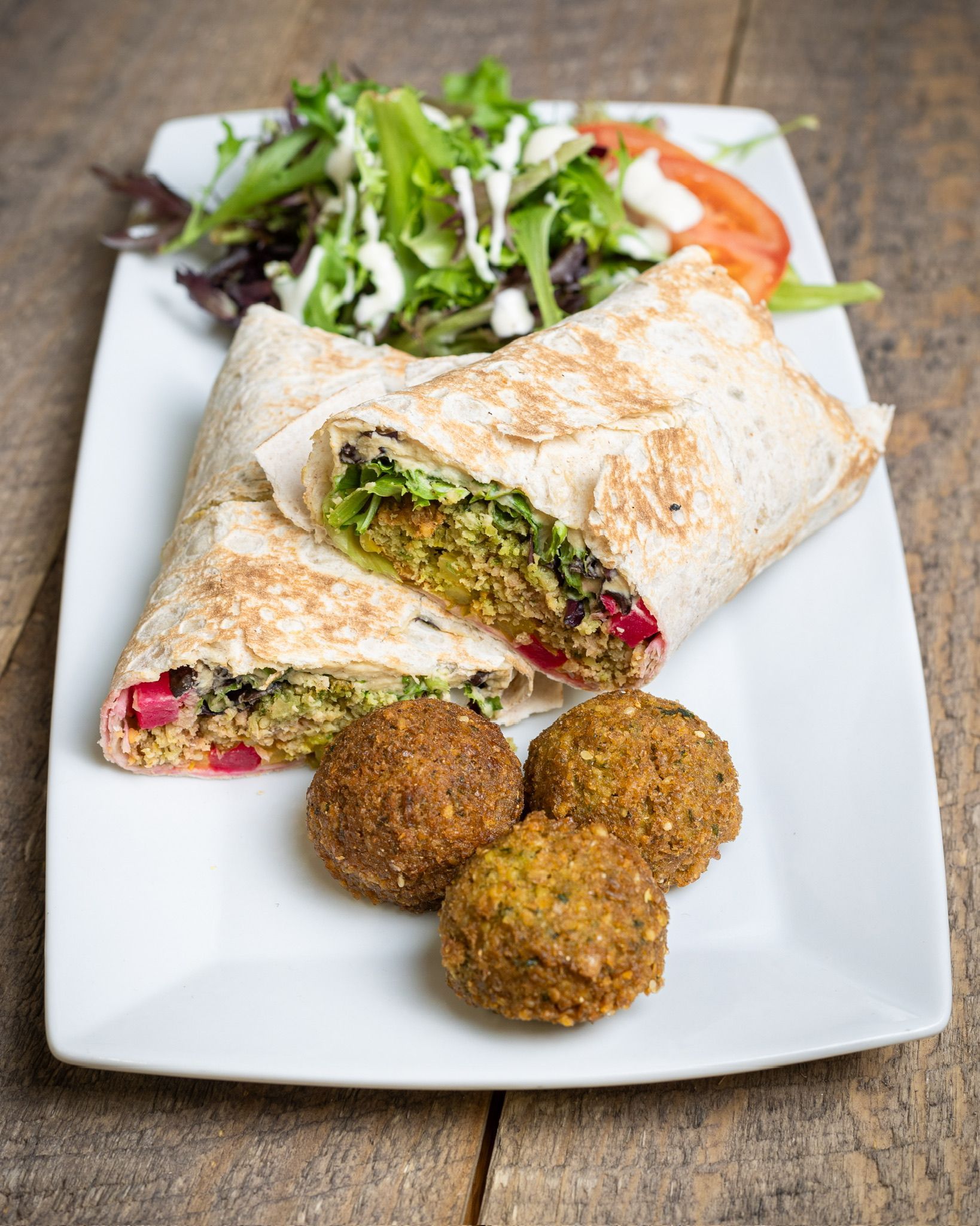 Falafel wrap cut in half with salad and falafel balls on a white plate.