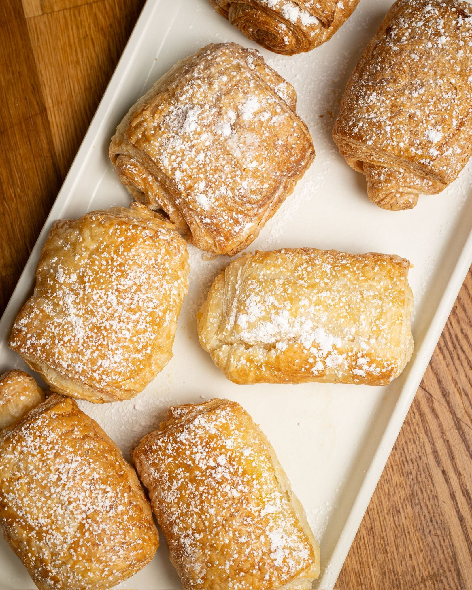 Pastries dusted with powdered sugar on a white rectangular plate, wood background.