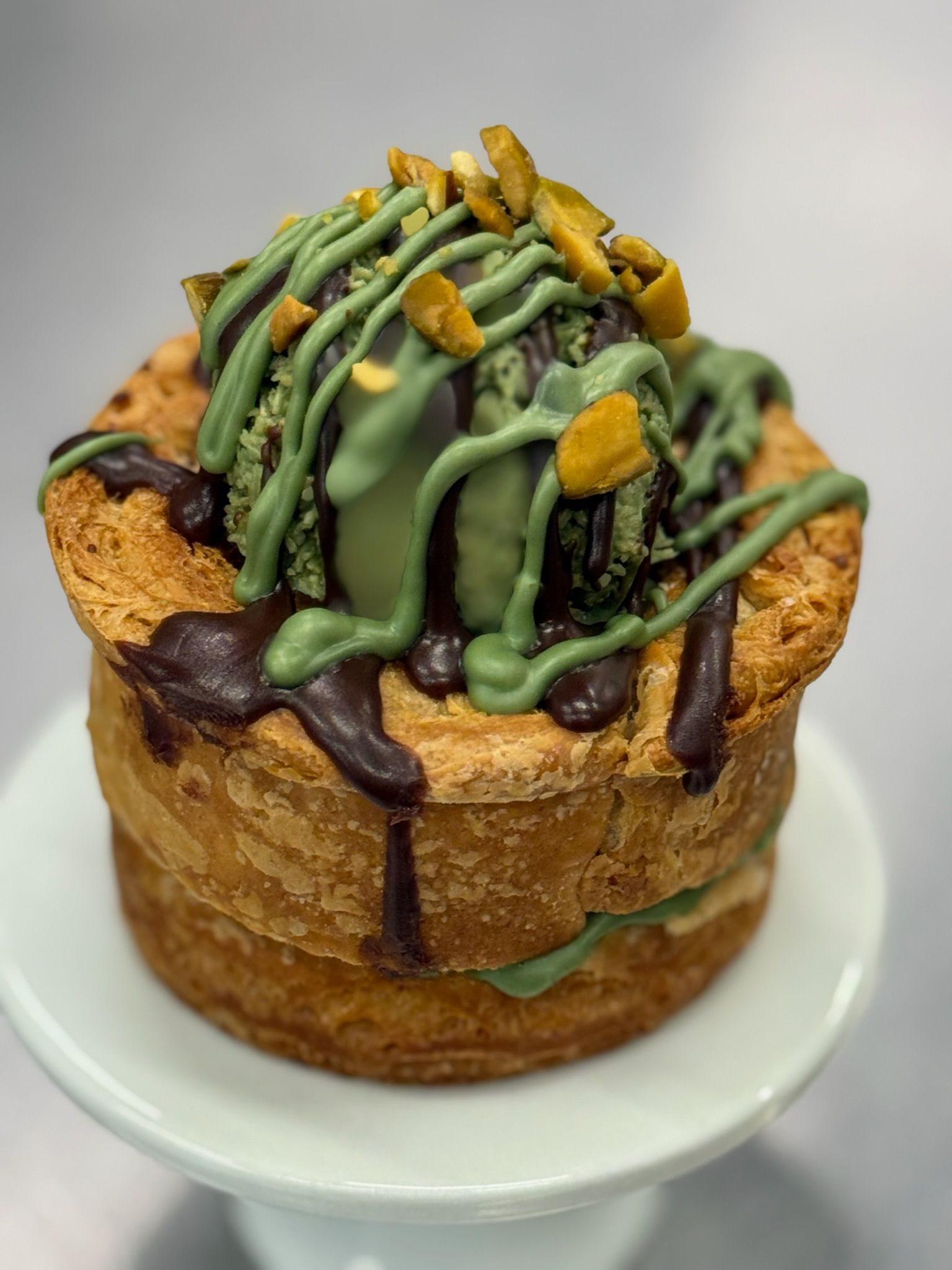 Pastry with matcha ice cream, drizzled chocolate and pistachio garnish.