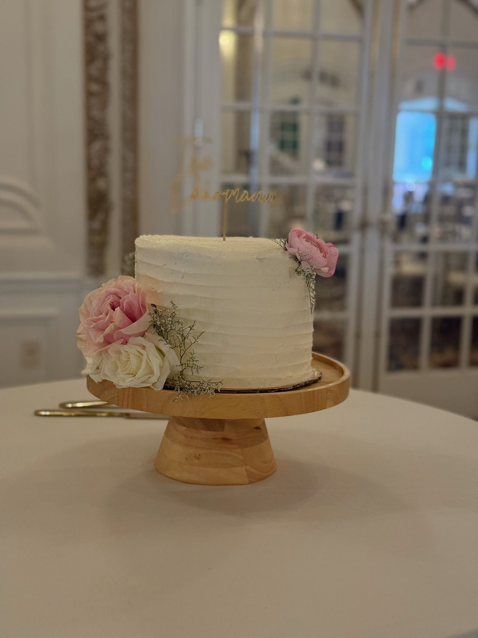 Wedding cake with flowers on a wooden stand. Set on a table with a blurred background.
