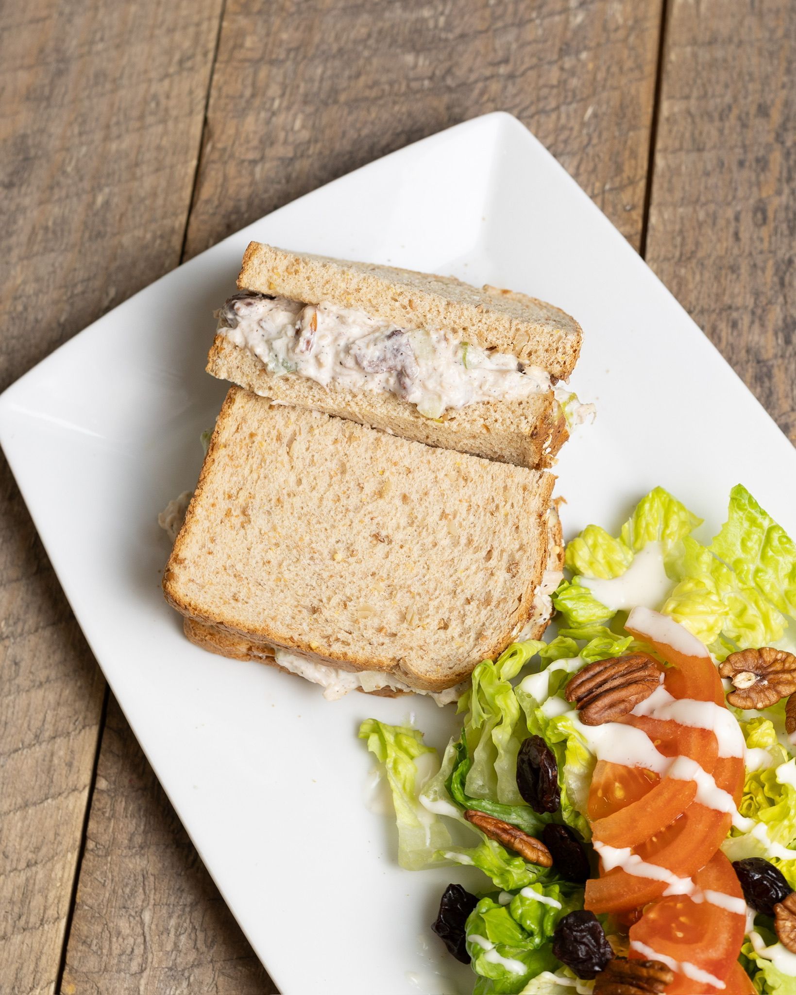 Chicken salad sandwich on wheat bread, with side salad of lettuce, tomato, pecans, and raisins.