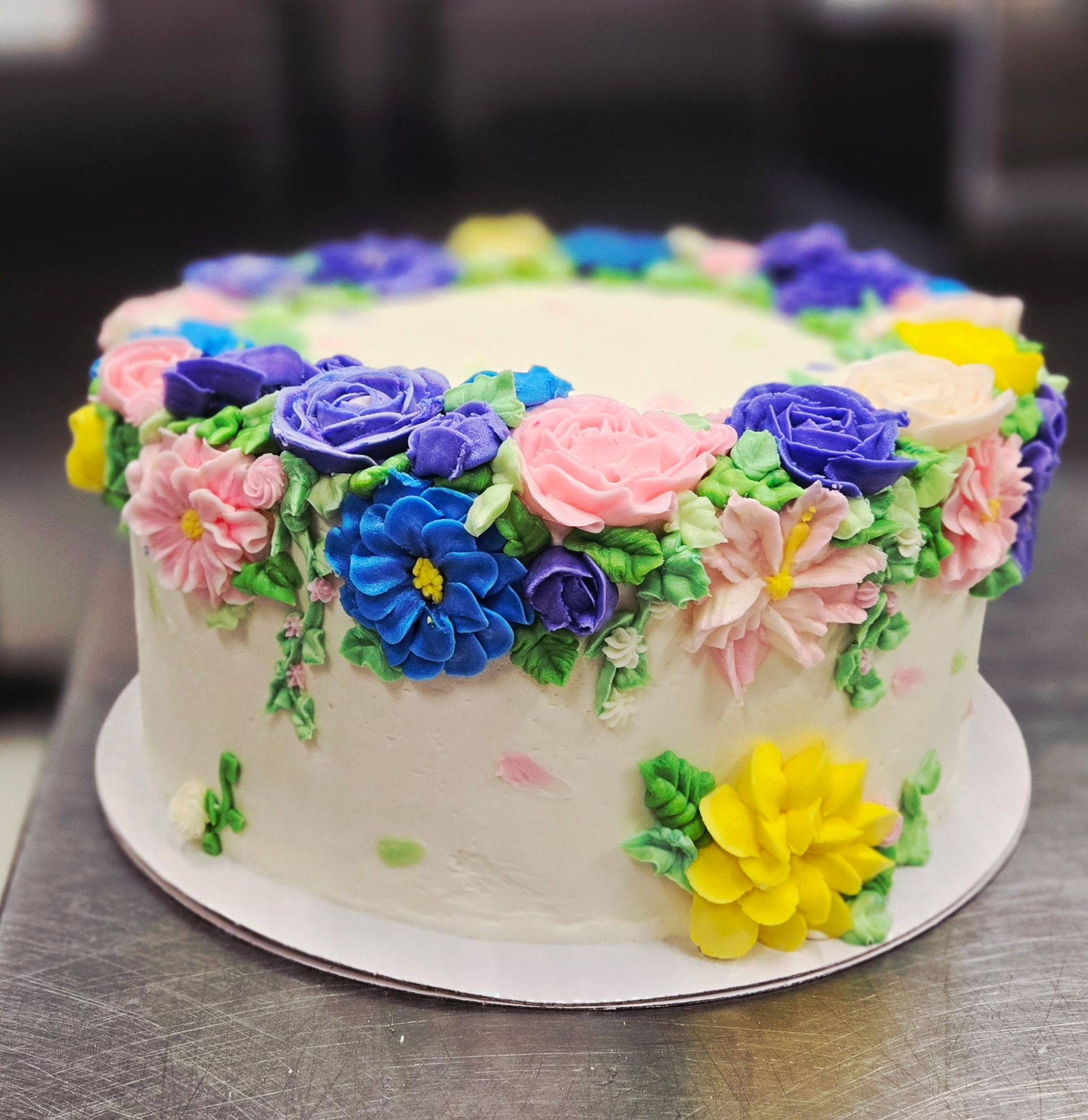 Cake with white frosting, decorated with colorful buttercream flowers in various shades.